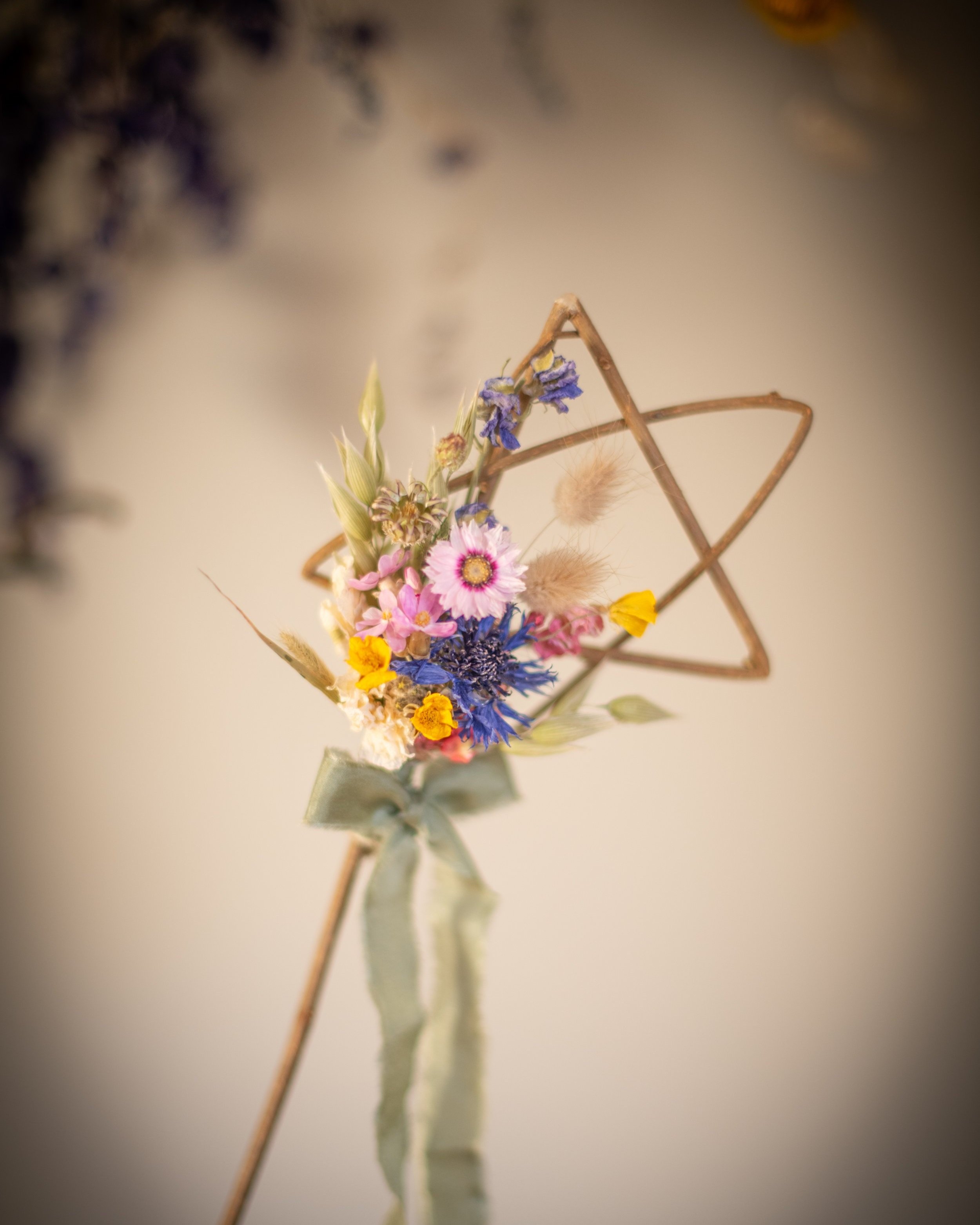 a star wand with dried flowers in a mix of natural colours and a wild flower feel. Finished with silk ribbons