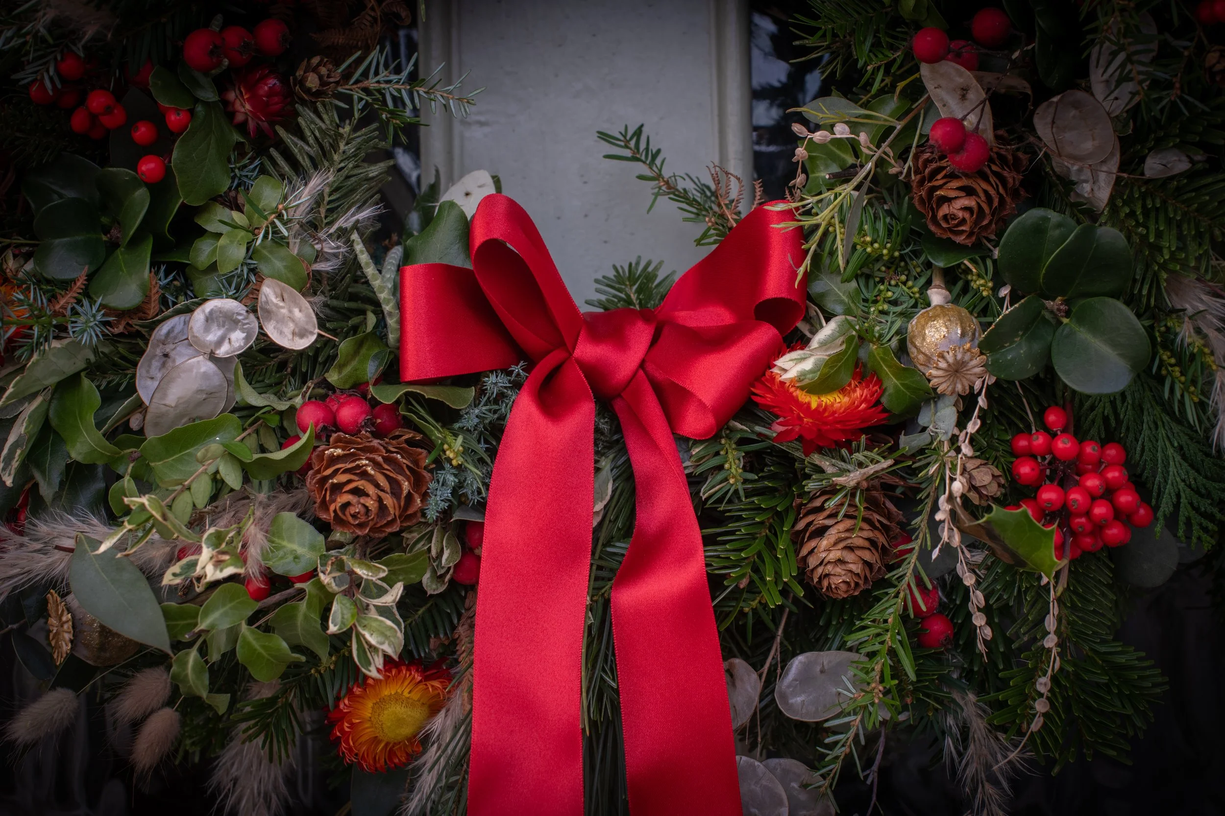 a beautiful, natural Christmas wreath filled with textures and colour from evergreen foliage, dried flowers, berries and fir cones finished with a glossy red ribbon.