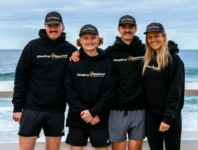 Run Australia team members Griffin JD Hughes, Flin Cobley, Chelsea Dyer and Nathan Maufe standing together in Destiny Rescue clothing by the coast.