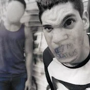RackaRacka youtube logo A young man is making a funny face with handwriting on his cheek, while another person stands nearby with their arm partially visible.