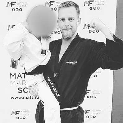 A young girl in a martial arts uniform standing next to an adult man in a martial arts uniform, both smiling and flexing their arms. Children’s faces blurred for privacy.