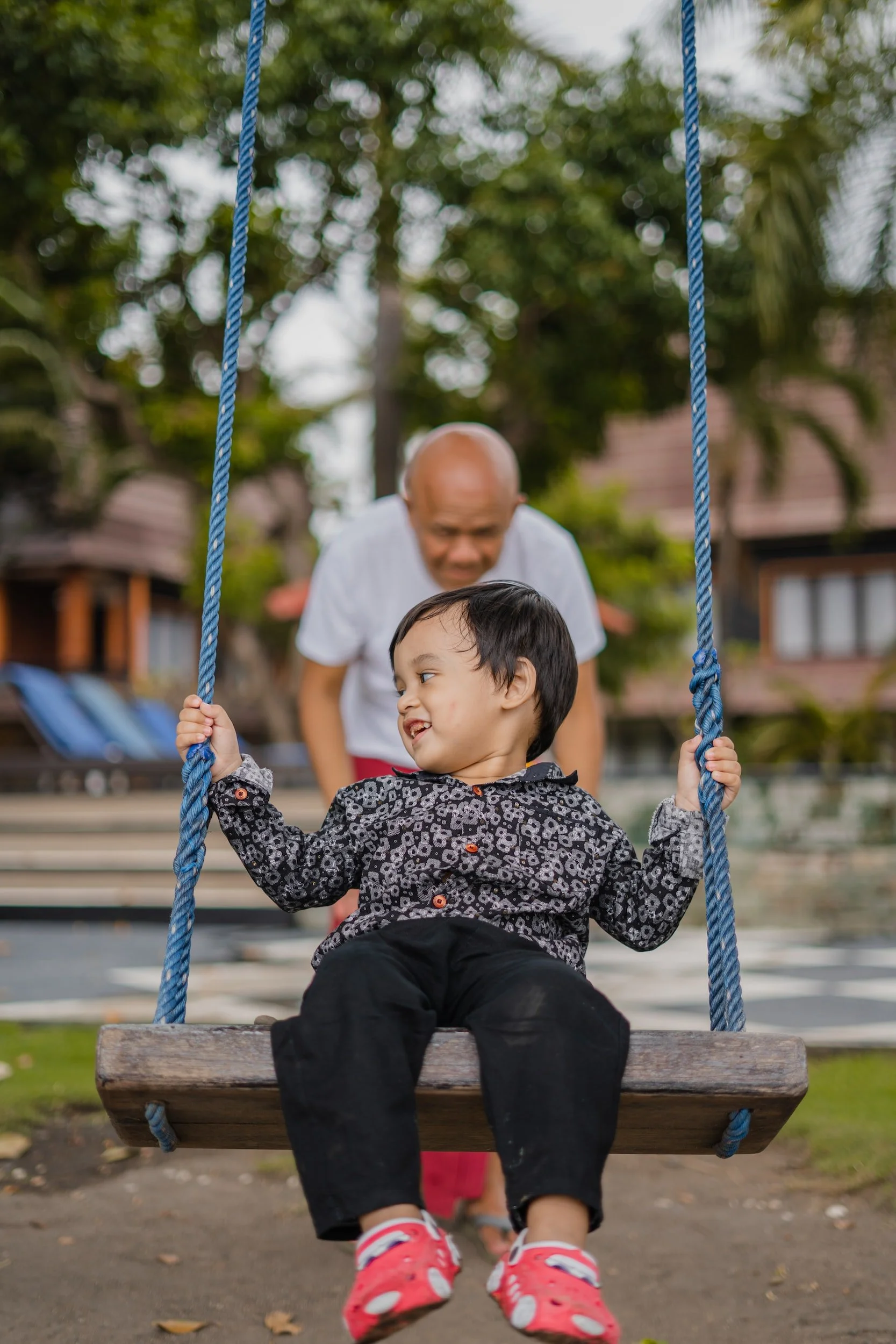 Photo of a small child swinging and smiling, being pushed by their grandpa.
