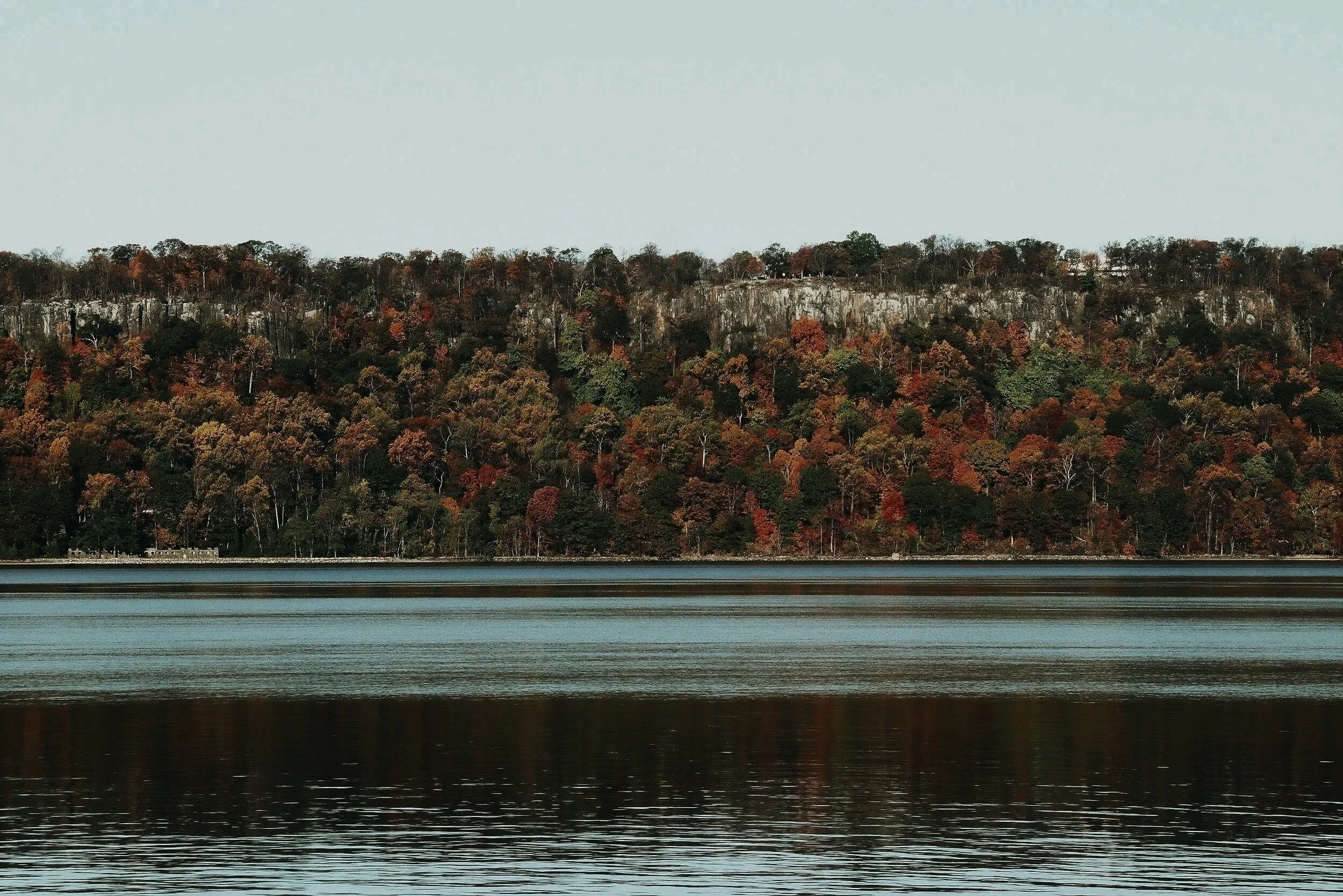 A lake with a forested hill in the background, showing autumn foliage.