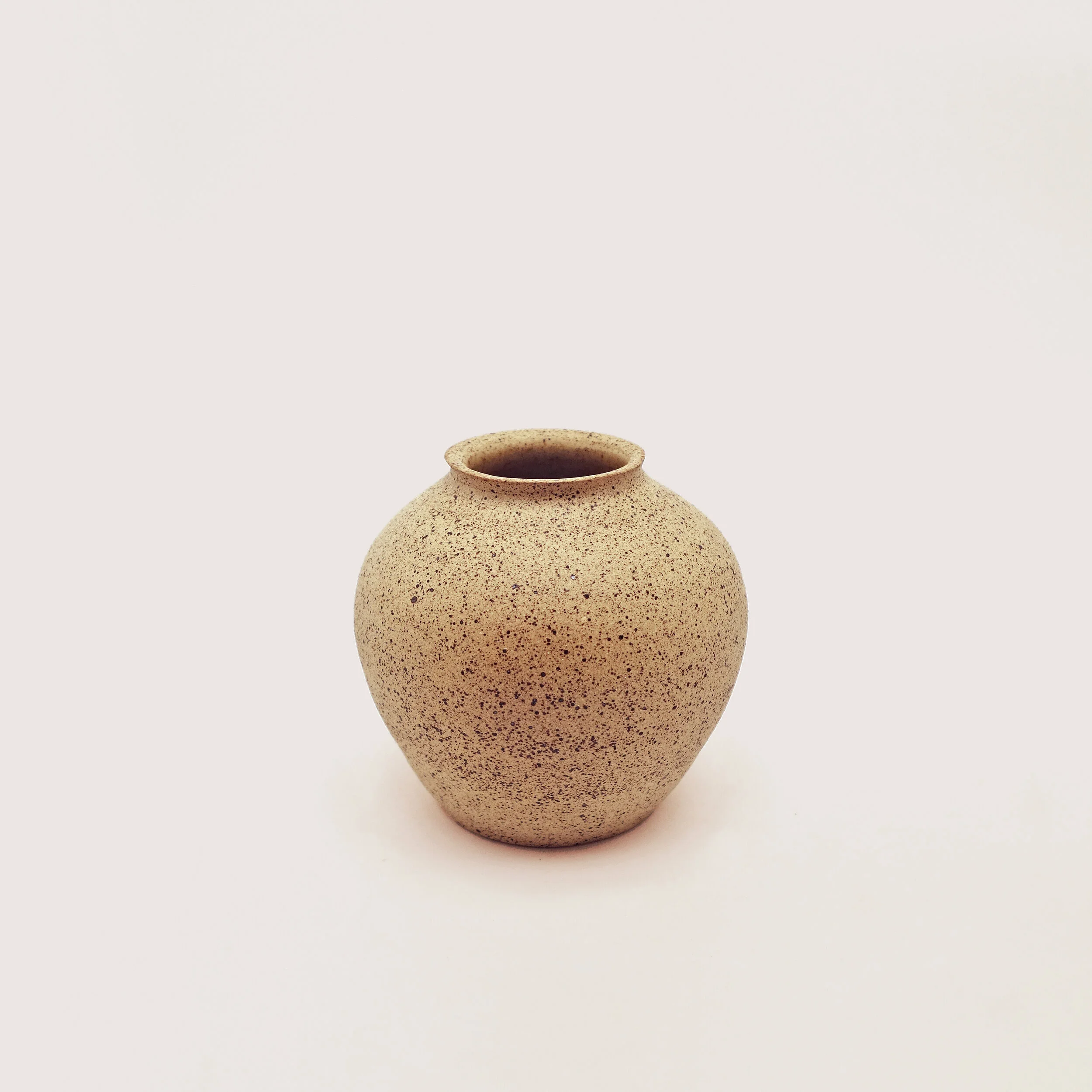 Eine sandfarbene Vase mit einem schmalen Hals und runder Form.