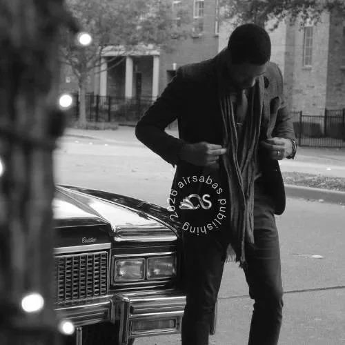 Korey Larkins wearing a suit from Suit Supply standing next to a car on a street at night, adjusting his coat or shirt.
