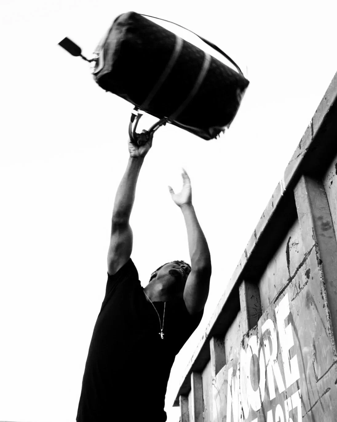 Malcom 'Lamborghini' Smith tossing a large Louie Vuitton duffle bag outdoors, into a waste bin with graffiti.