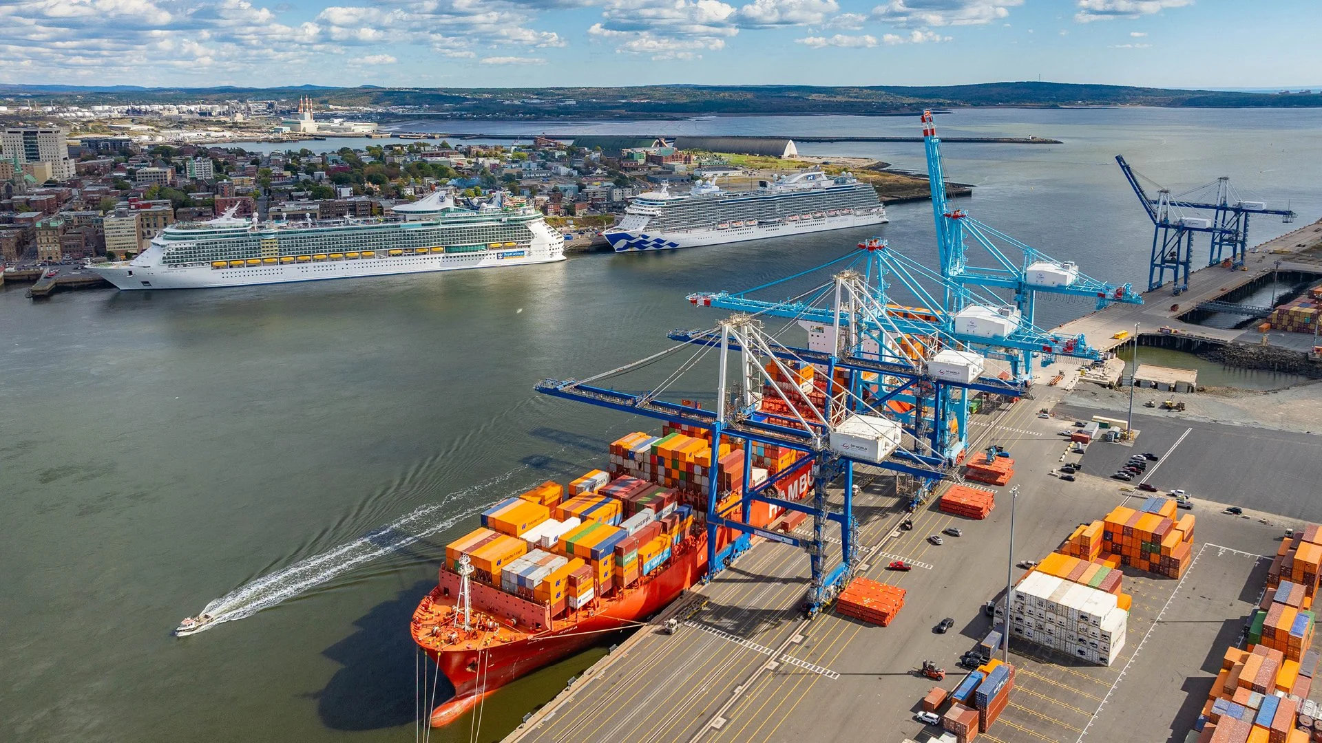 Aerial view of Port Saint John featuring a large container ship docked at the terminal with two cruise ships in the background.