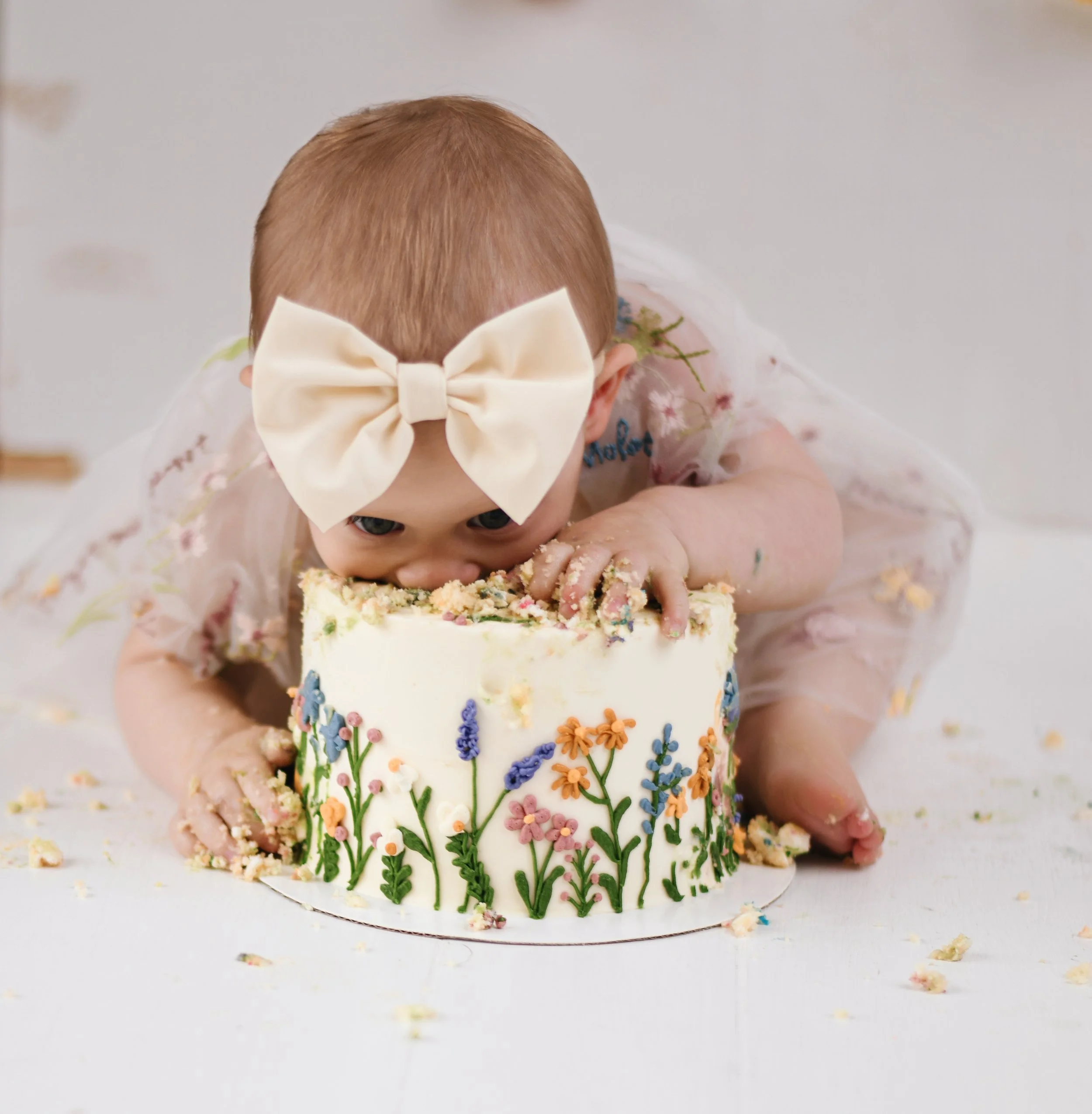 Child with a large bow headband eating a decorated birthday cake with floral icing design.