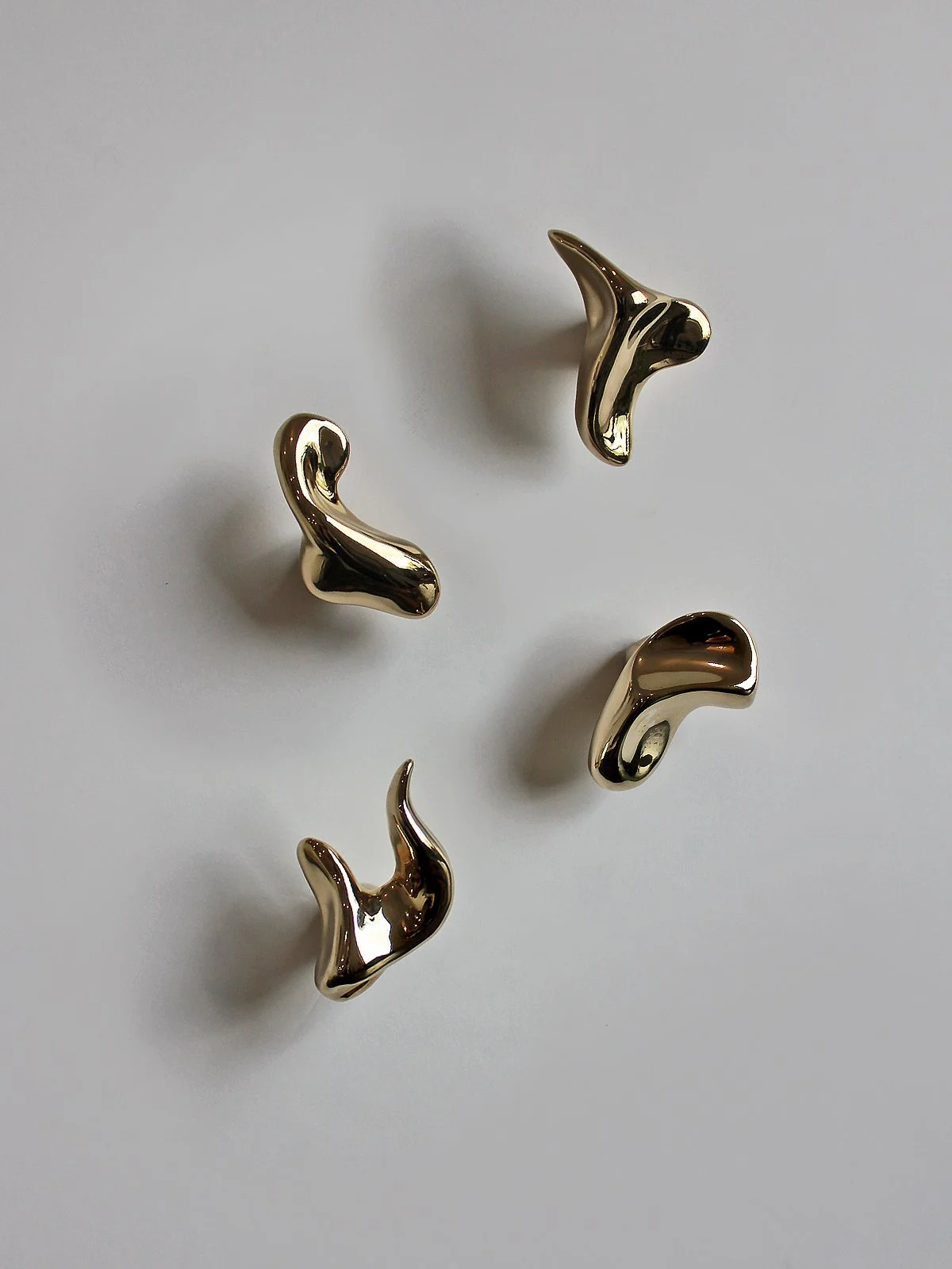 Five sculptural brass shiny gold hooks on a white wall.