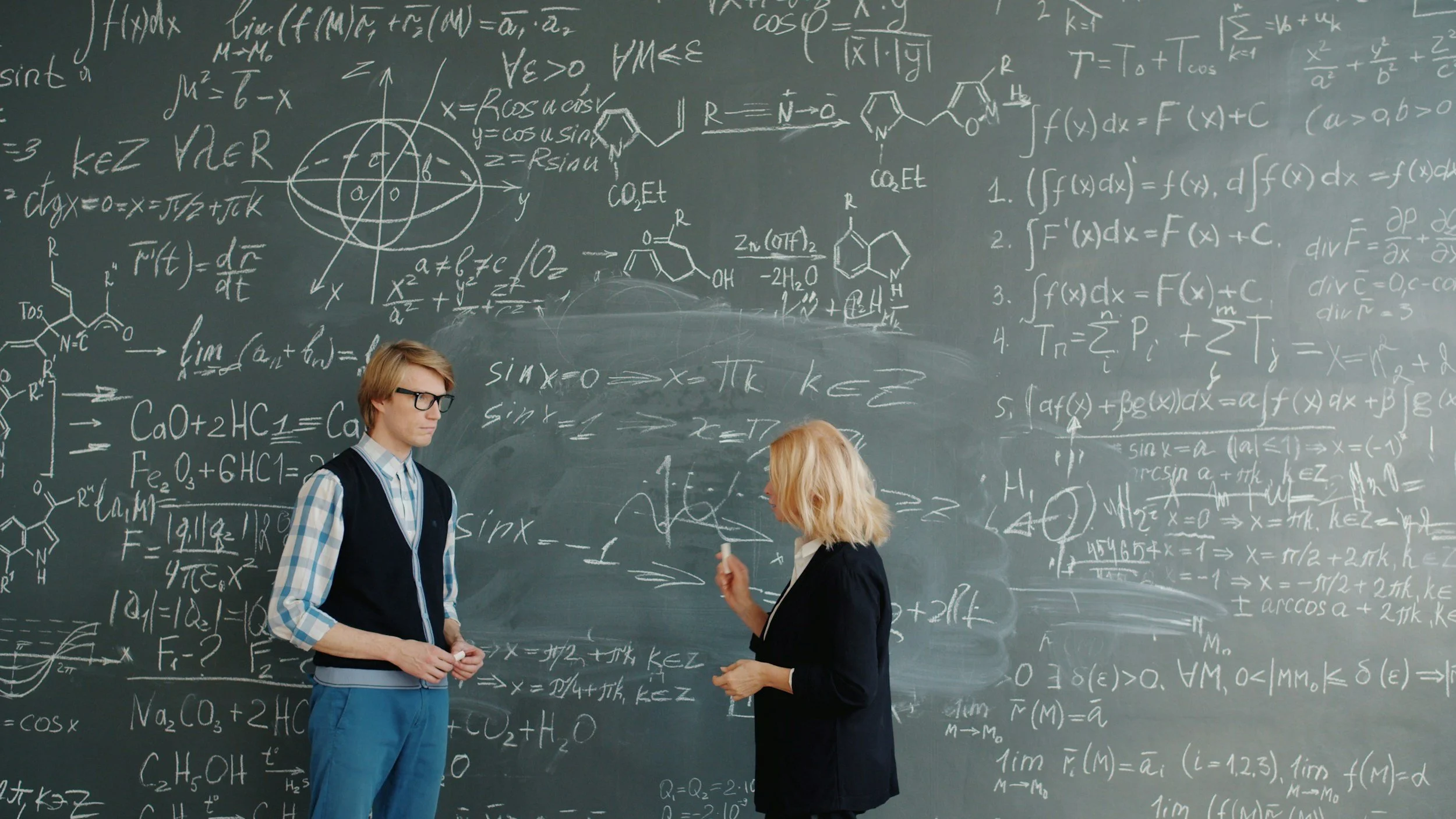 Student and teacher talking about SAT math problems in front of chalk board