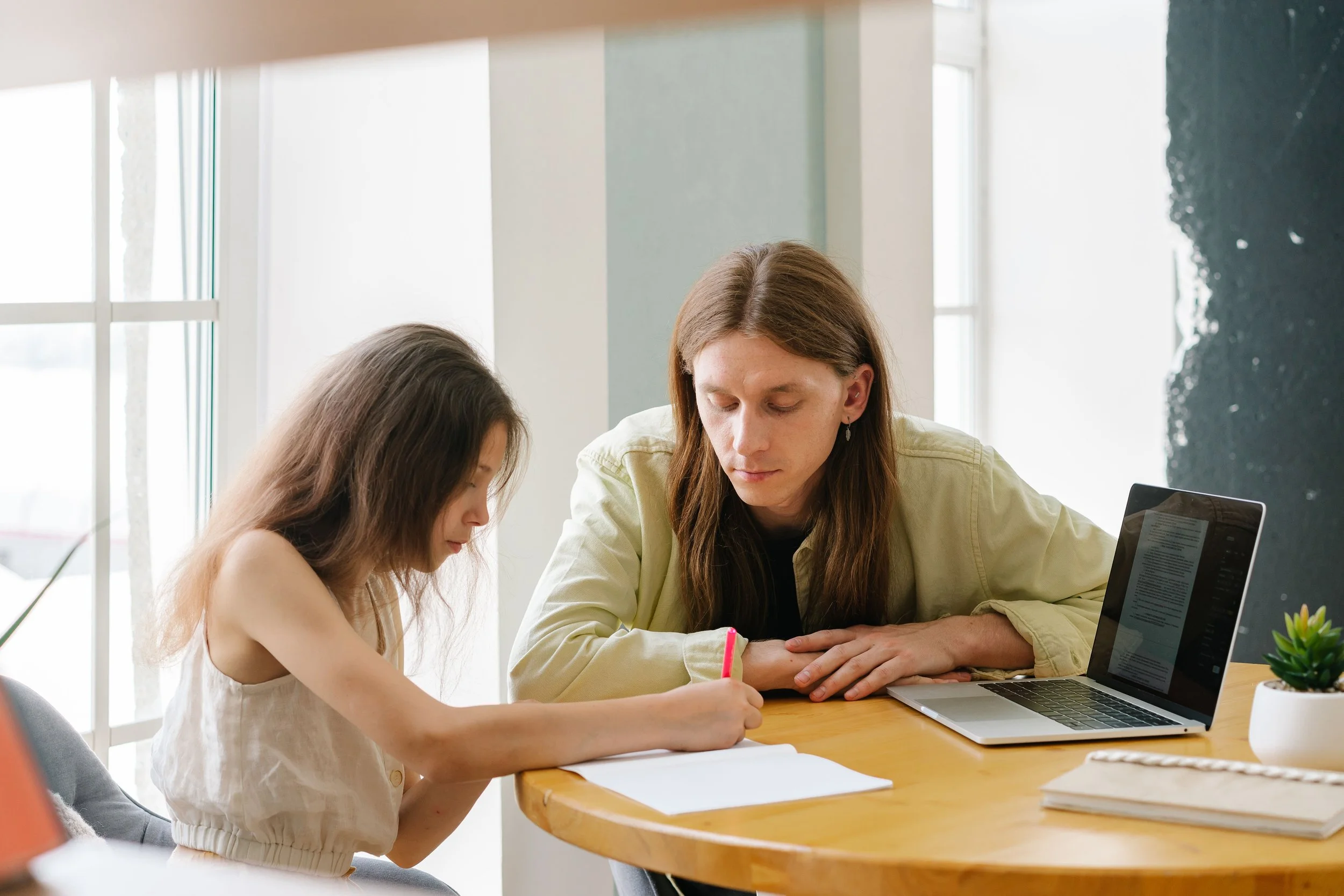 Tutor helps student write essay at table with laptop open
