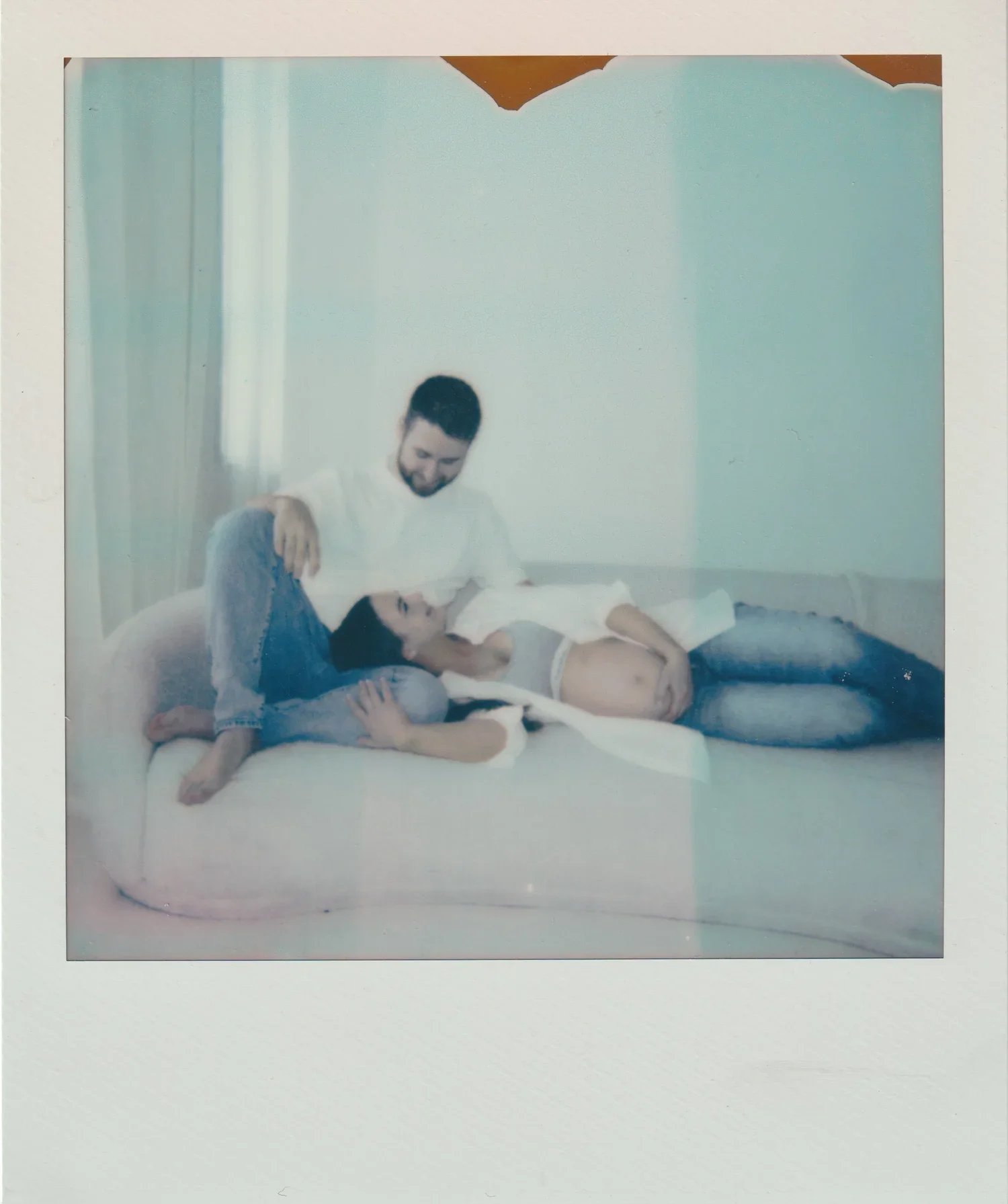 Two people engaging in a playful pillow fight on a bed in a room with light-colored walls and curtains.