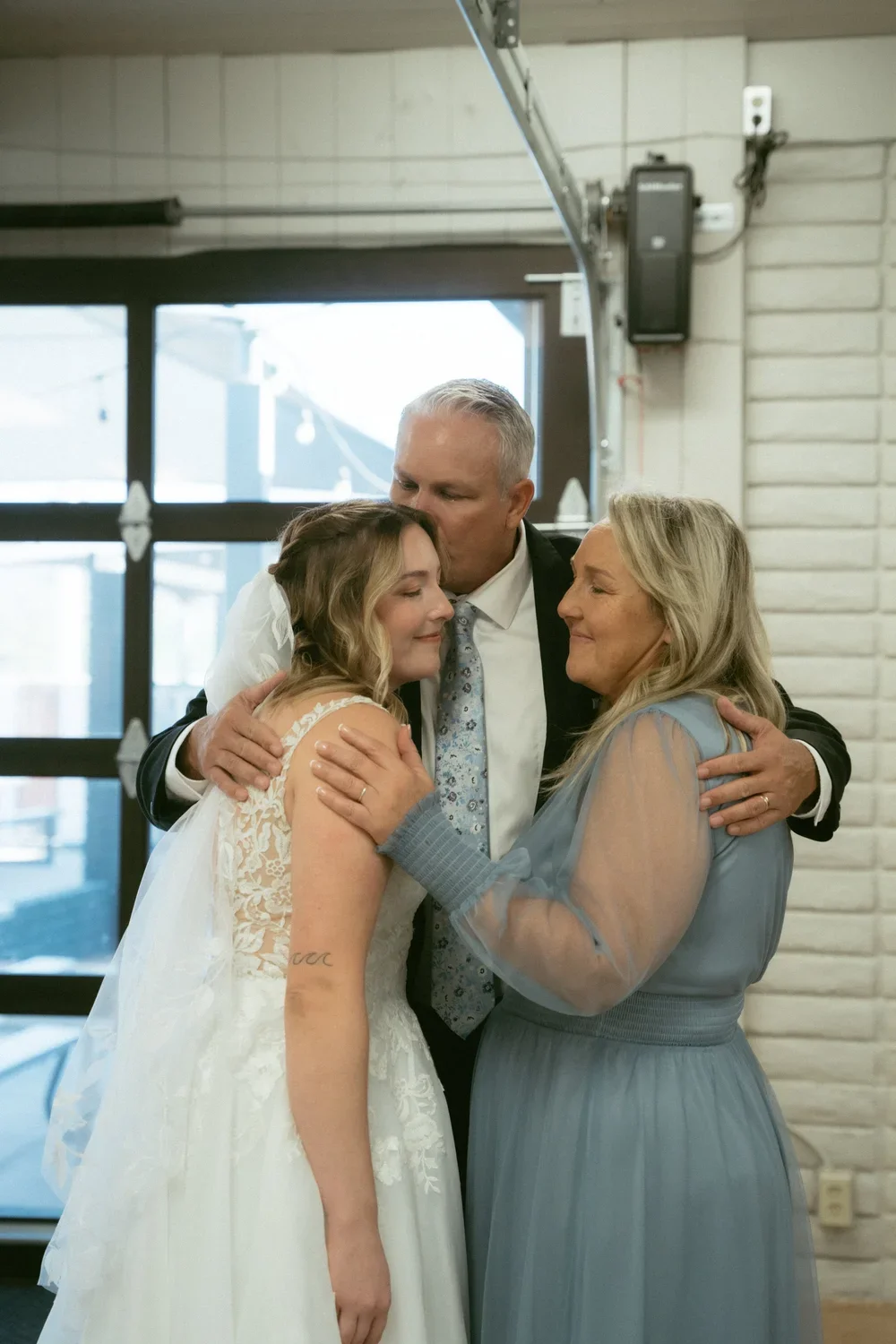 A bride and her parents sharing a warm hug at her wedding reception.