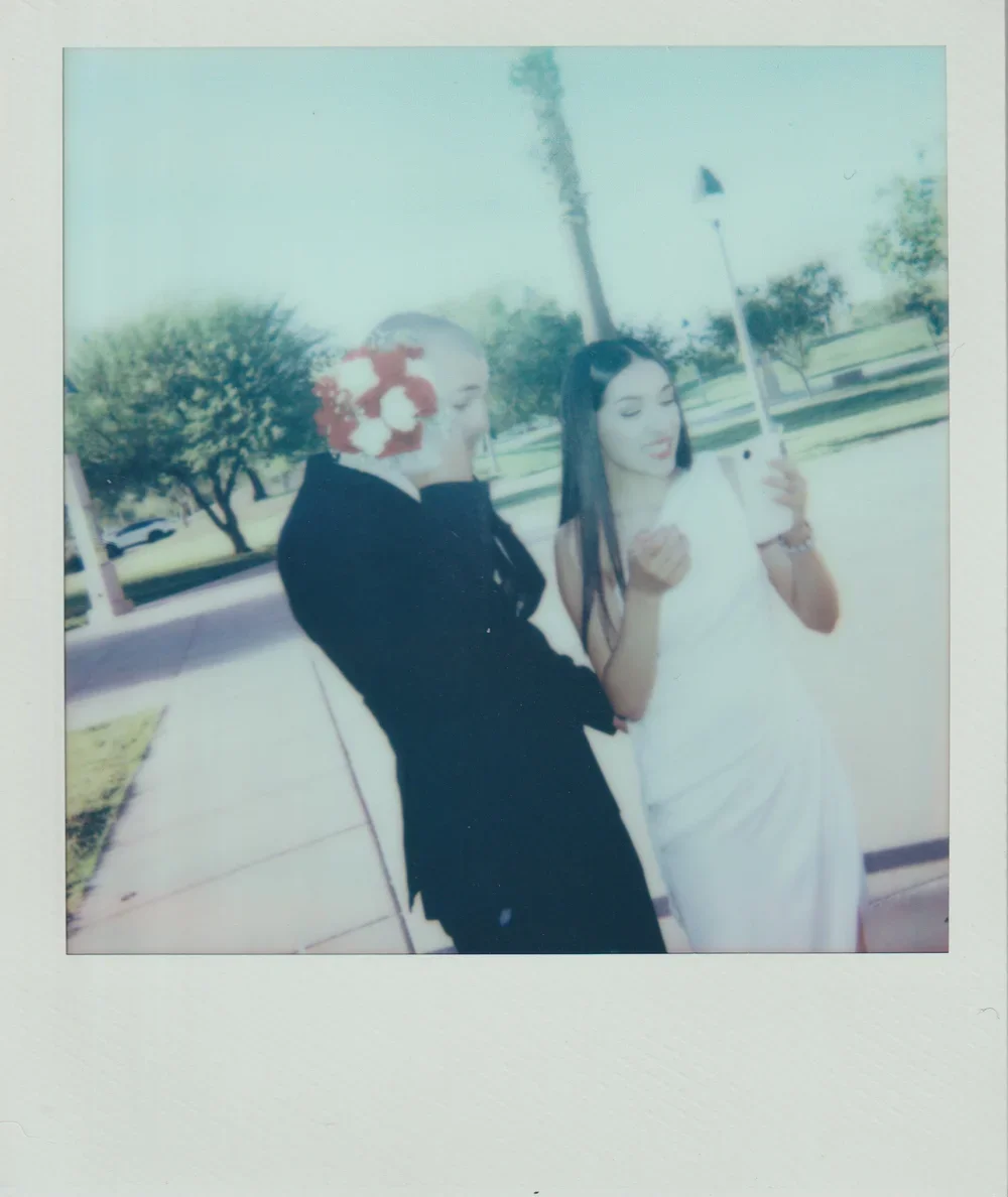 A woman in a white dress holding a golf club stands next to a woman in a black dress outdoors on a sunny day.