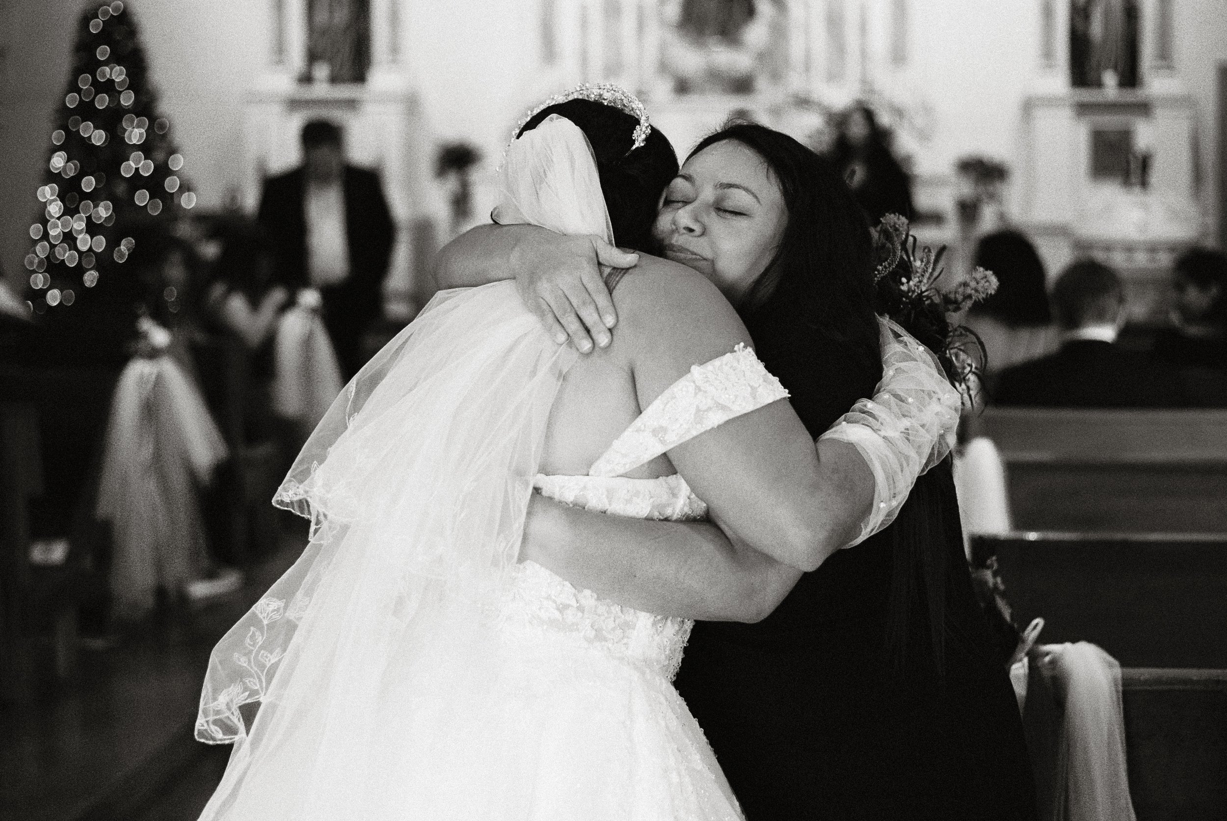A bride and another woman hugging inside a decorated church during a wedding celebration.