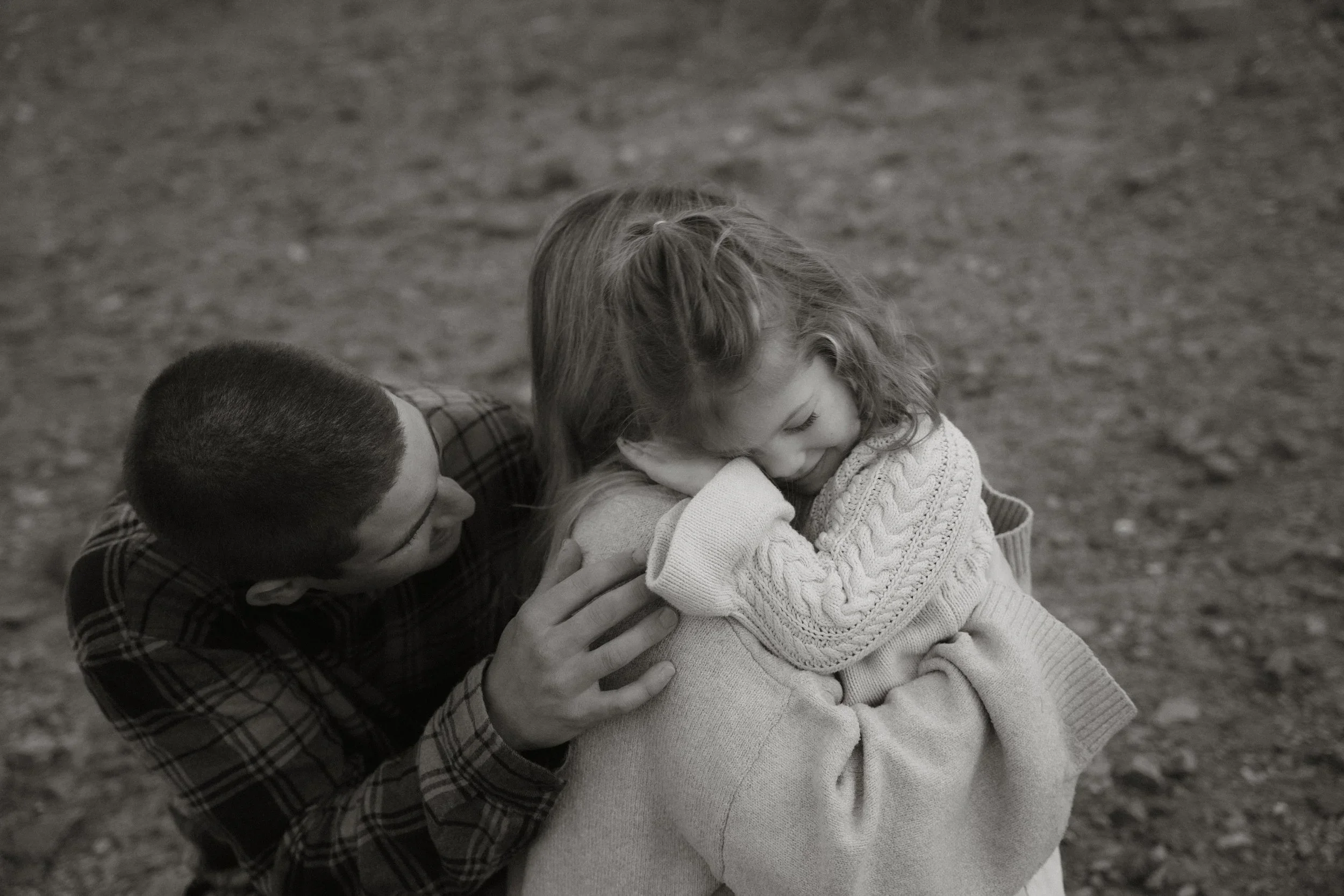 A man and a woman sharing a moment of joy outdoors. The man is smiling and the woman is laughing with her eyes closed, hugging her knees, in a black-and-white photo.