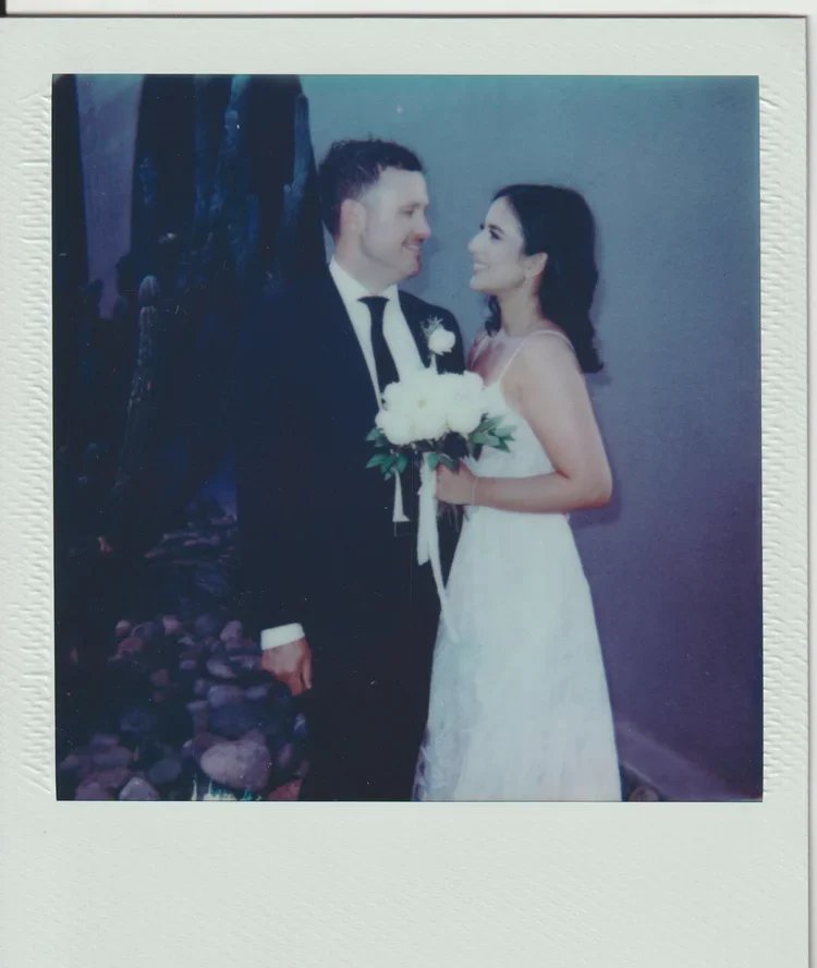 A bride and groom in wedding attire sharing a tender moment, with the bride holding a bouquet of white roses.