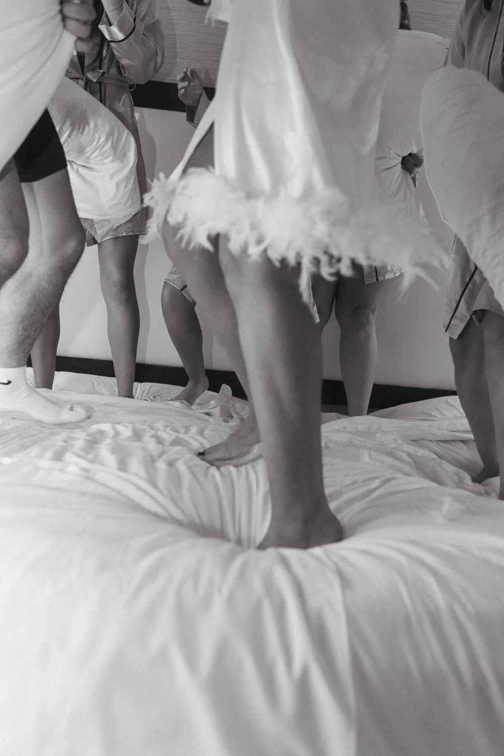 Group of people on a bed, standing and wearing pajamas, viewed from below and focusing on their legs and feet.