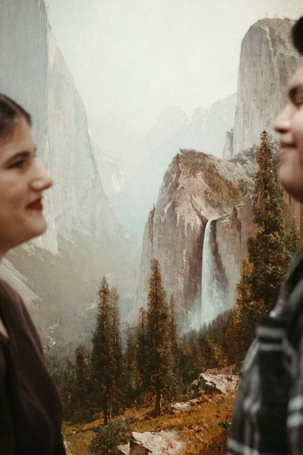 Two women face each other with a mountain and waterfall mural in the background.