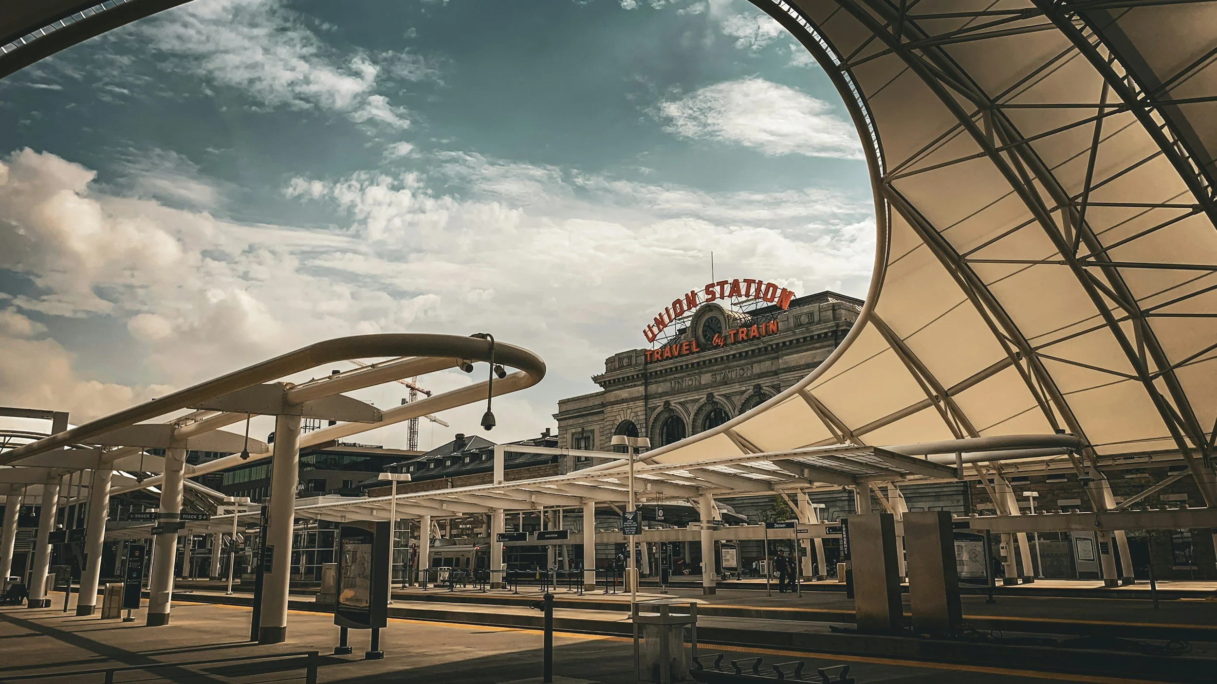 Union Station train platform with modern canopy, old building with neon sign, and a partly cloudy sky.