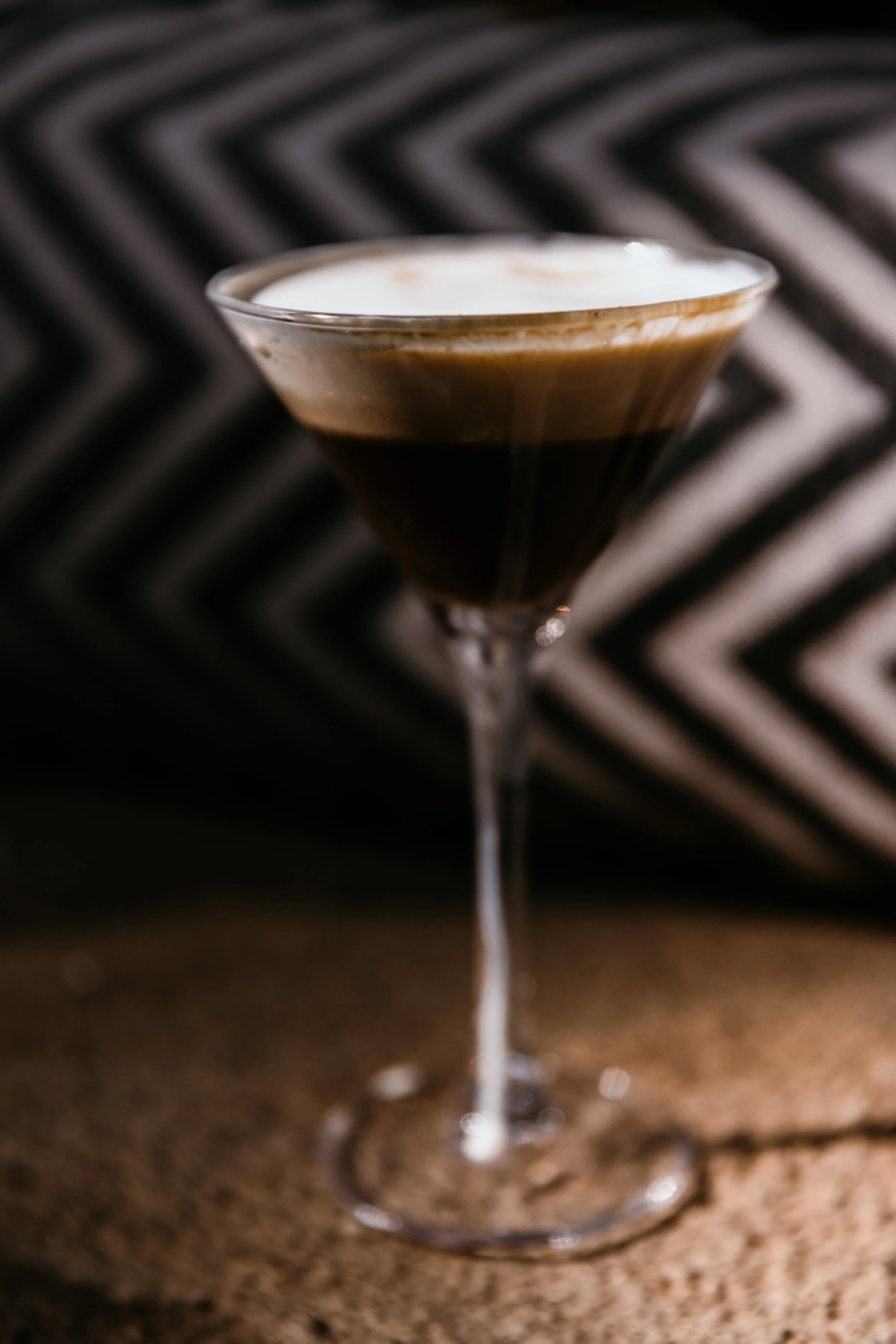 Espresso martini in a glass with frothy top, zigzag background