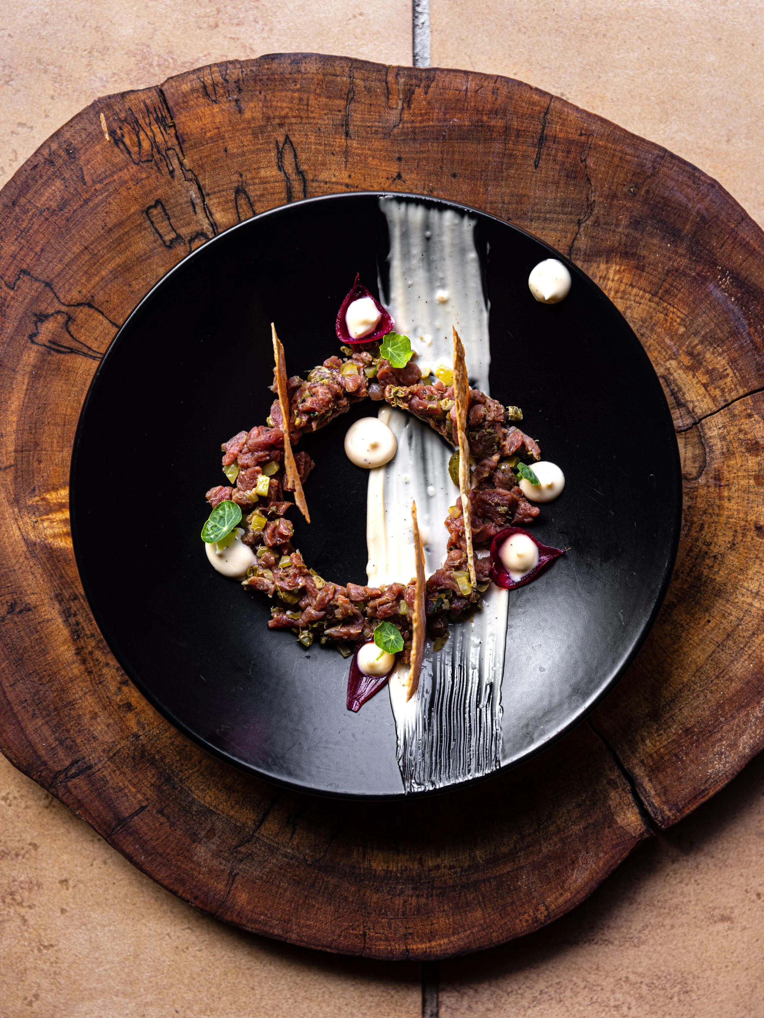 Gourmet beef tartare with garnishes on a black plate