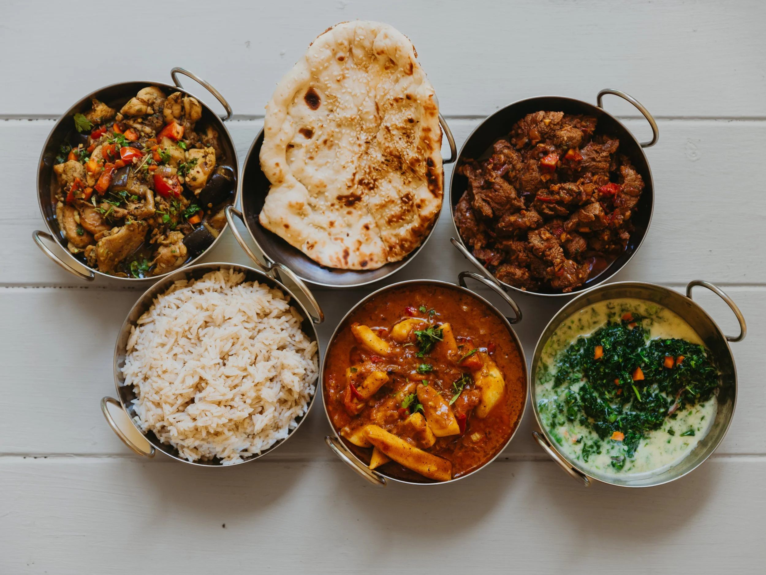 Assorted Indian dishes and naan bread on a light wooden table.