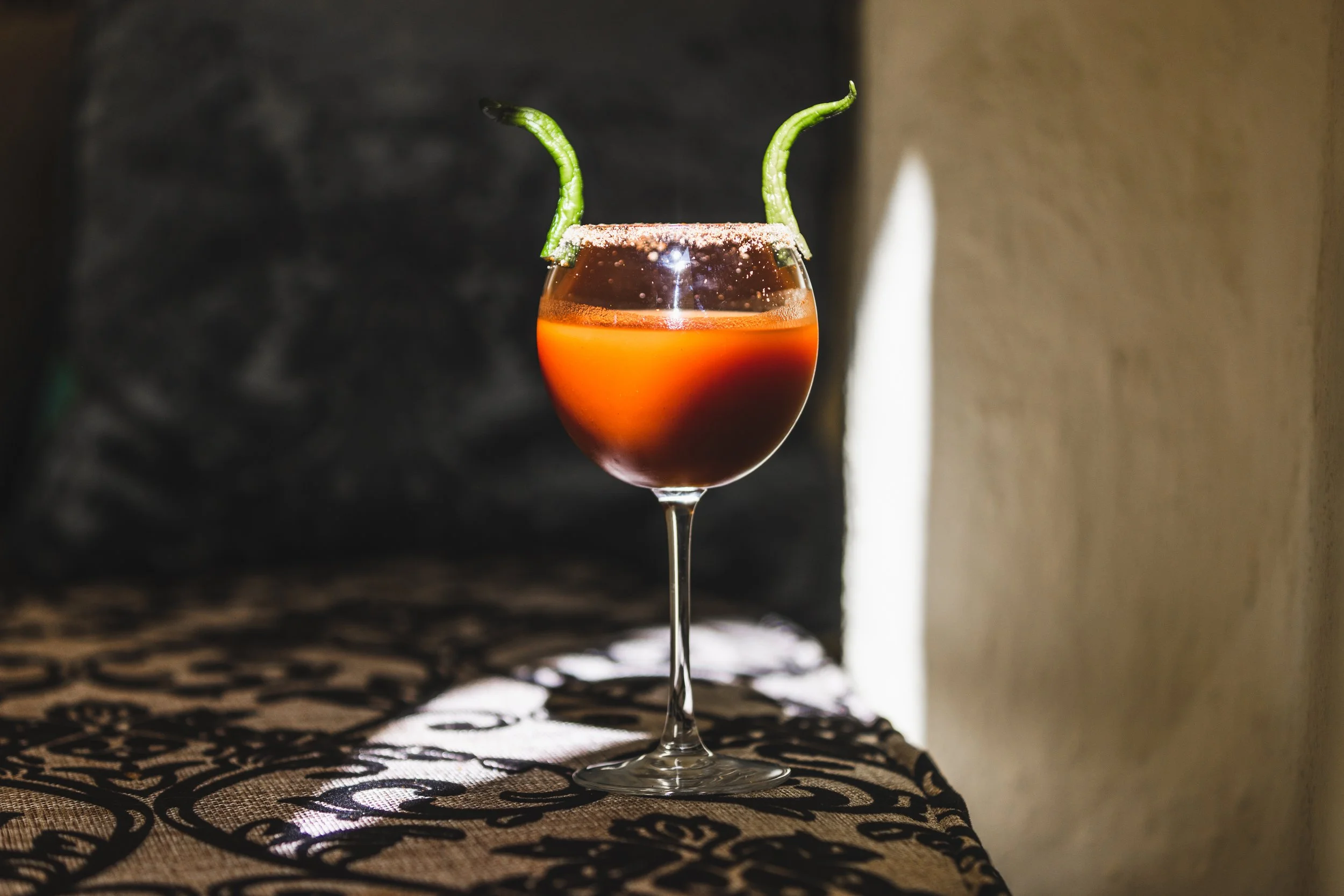Spicy cocktail in a wine glass with two green chili peppers as garnish.