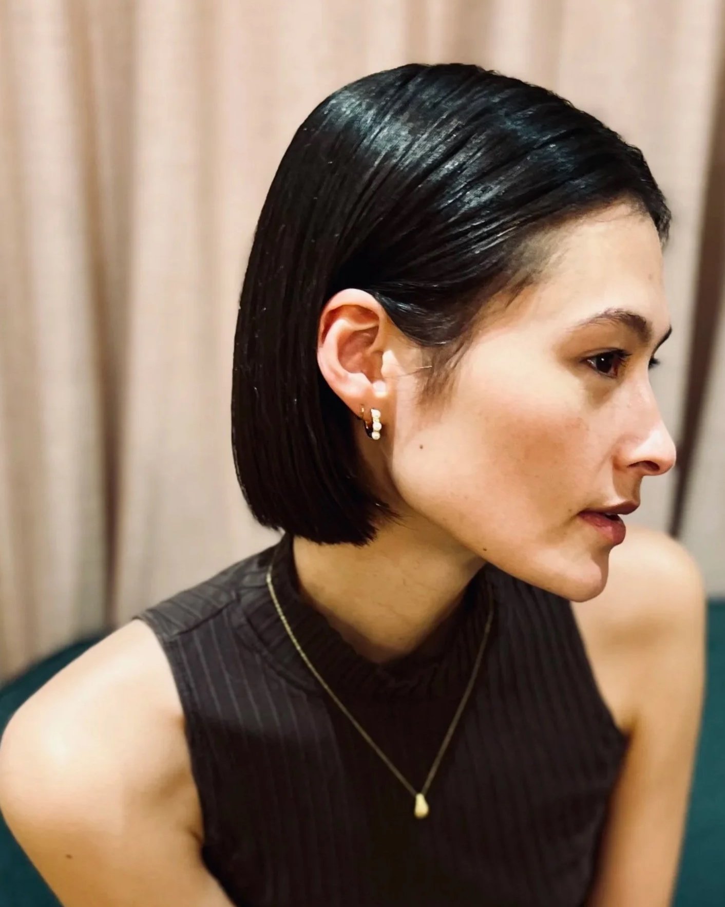Side profile of a woman with a sleek, dark brown bob haircut, wearing a brown animal print top, against a green background.
