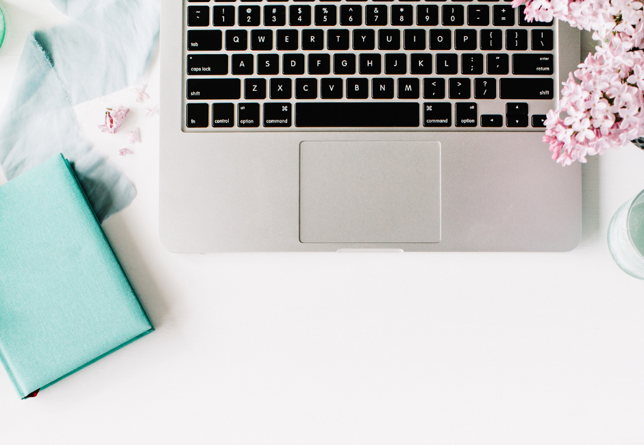 Laptop next to blue notebook and pink flowers
