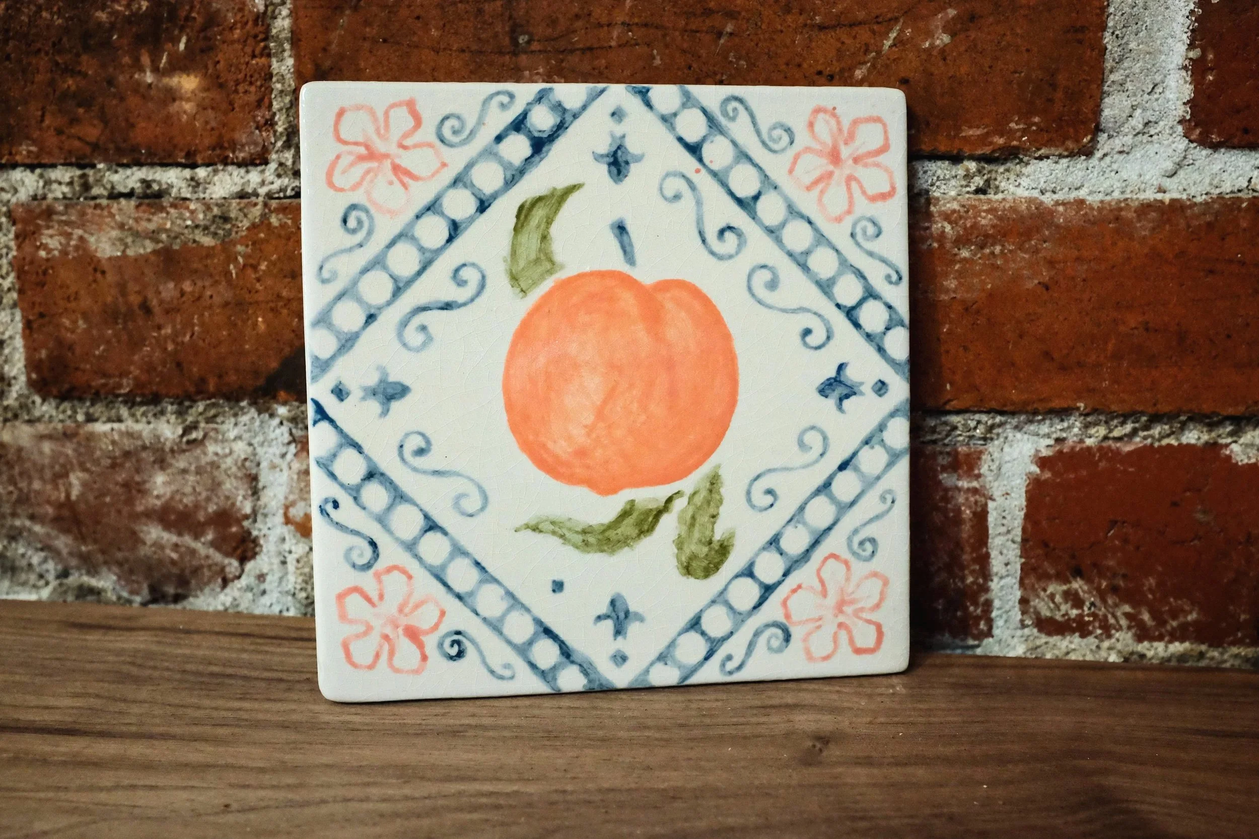 Decorative azulejo tile with a peach featured in the center and ornamental floral patterns around it.
