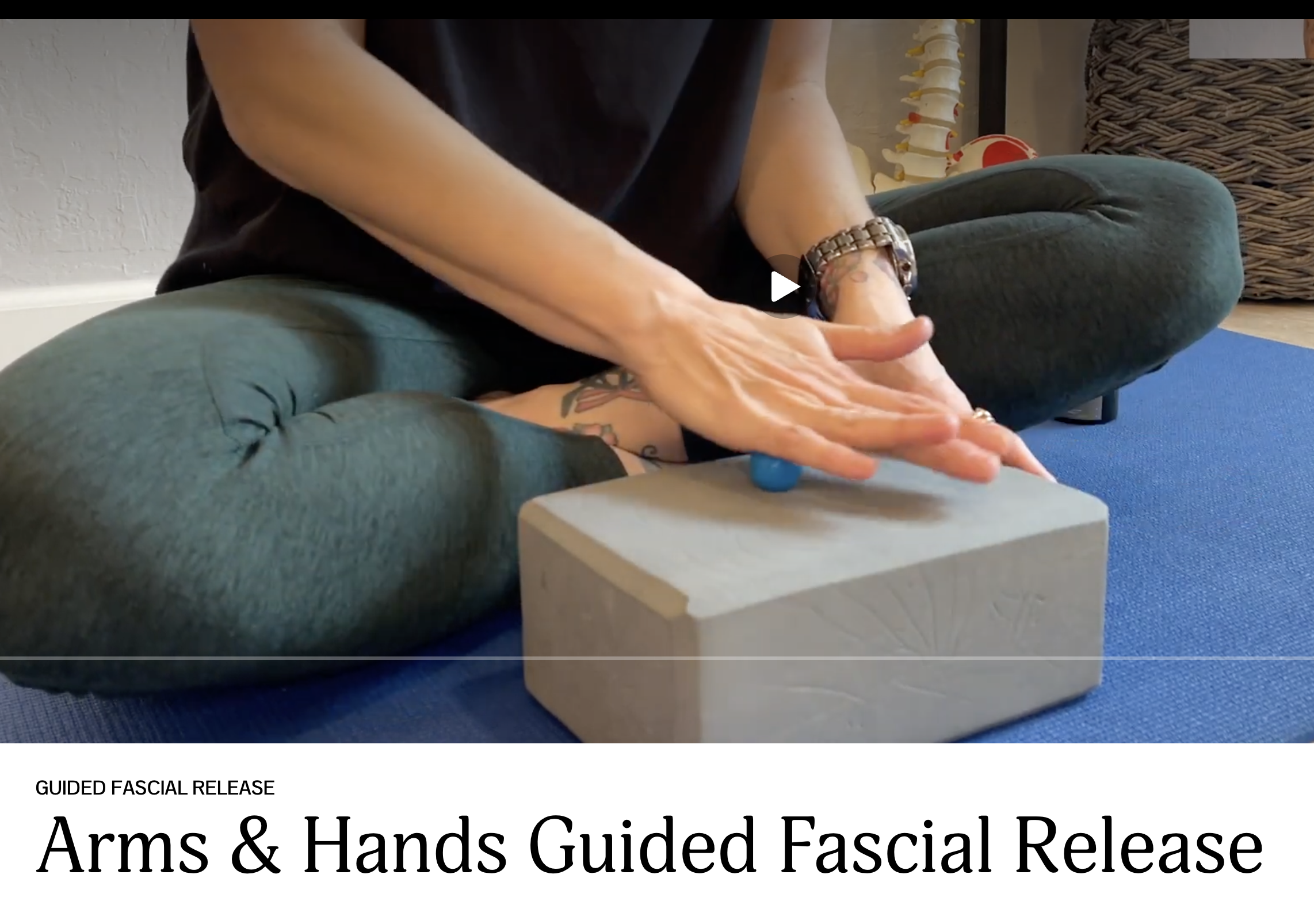 The image shows a person performing a guided facial release technique, with their hands on and around a person's face, who is lying down on a blue mat. The person has tattoos on their arms and wears a watch. The scene includes a model of a human spine and a weaving basket in the background.