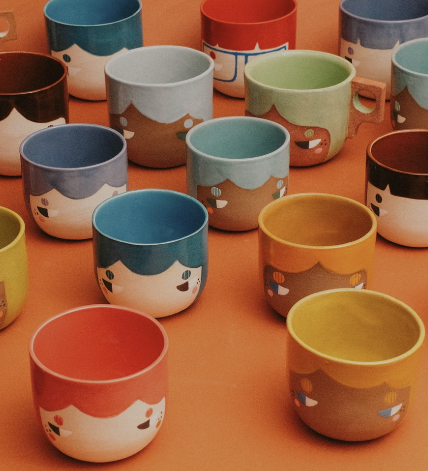 Colorful ceramic cups with cartoon face designs arranged on an orange surface.