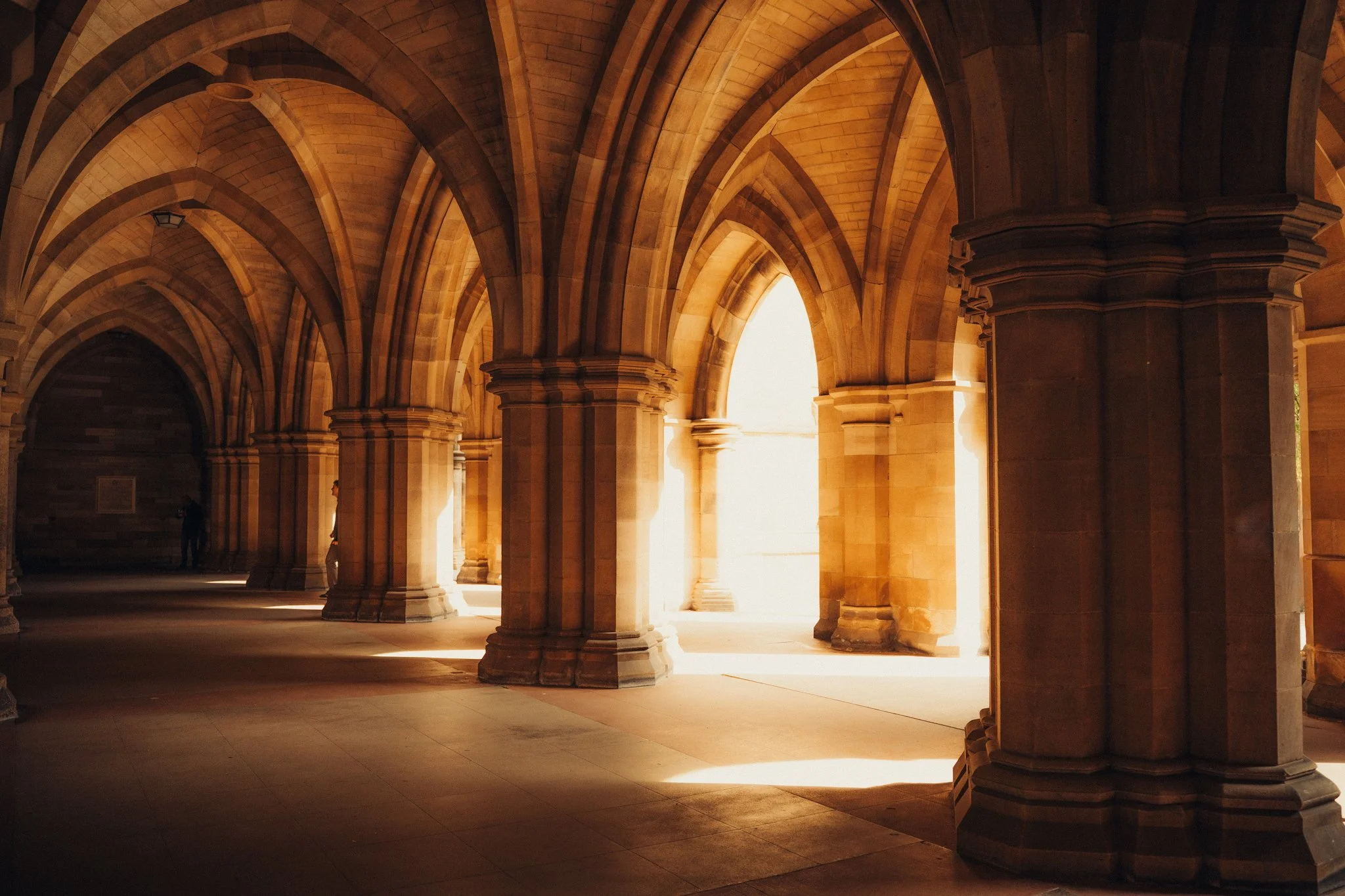 Sunlit stone arches and columns in a historic building corridor.