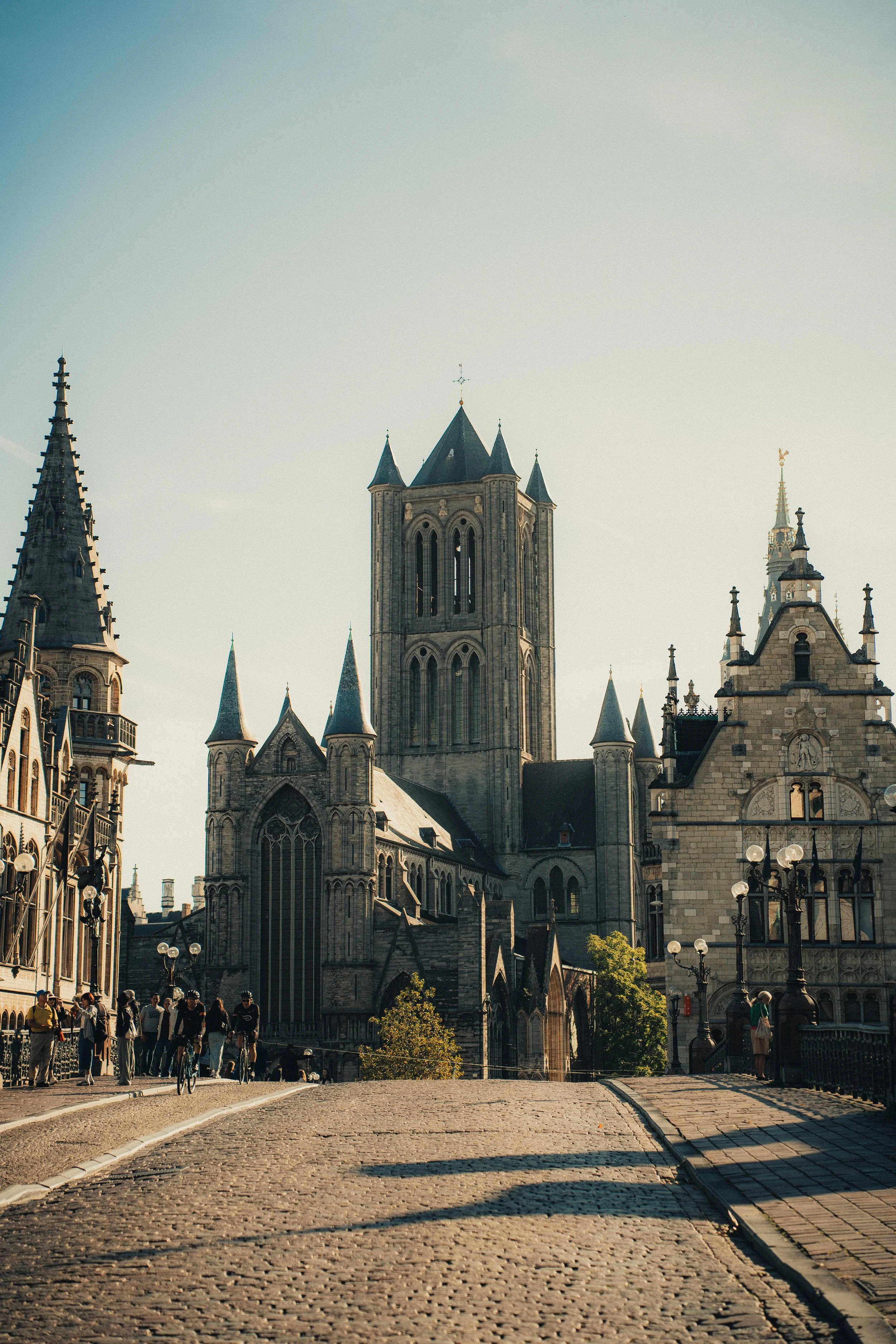 A cobblestone street leading to a Gothic-style cathedral with tall spires, surrounded by historic buildings and street lamps, in daylight.