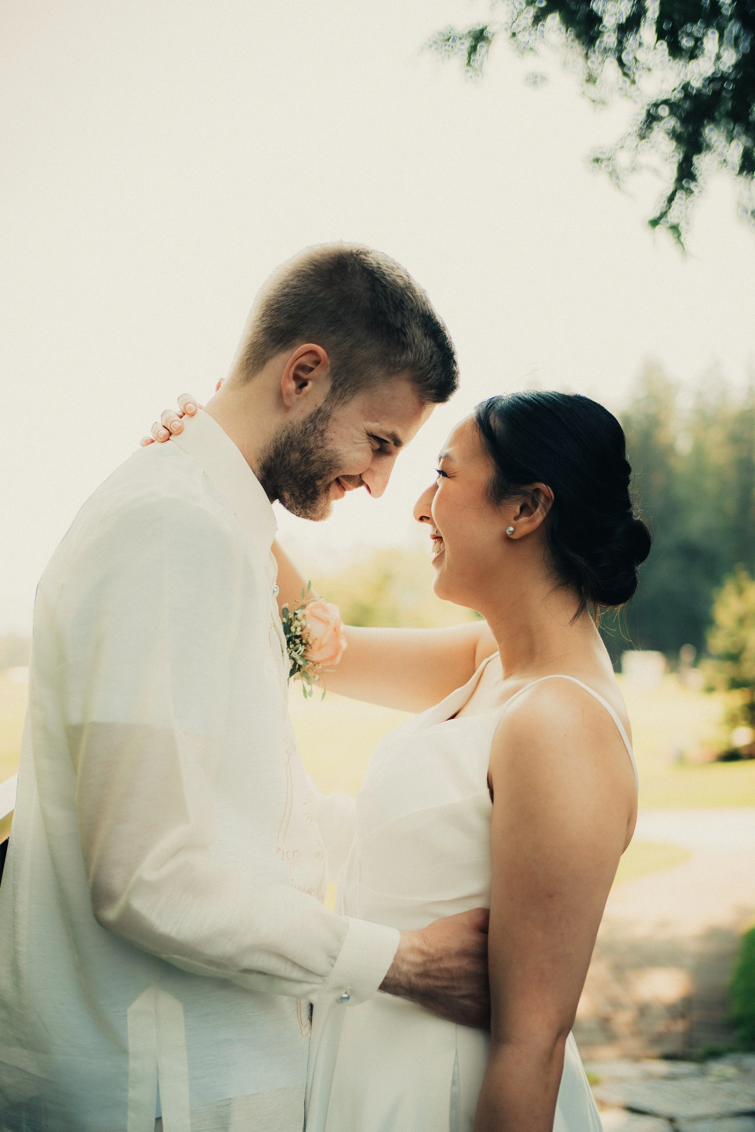 A happy couple, a man and a woman, are close together outdoors, smiling and touching foreheads, with a green park background.