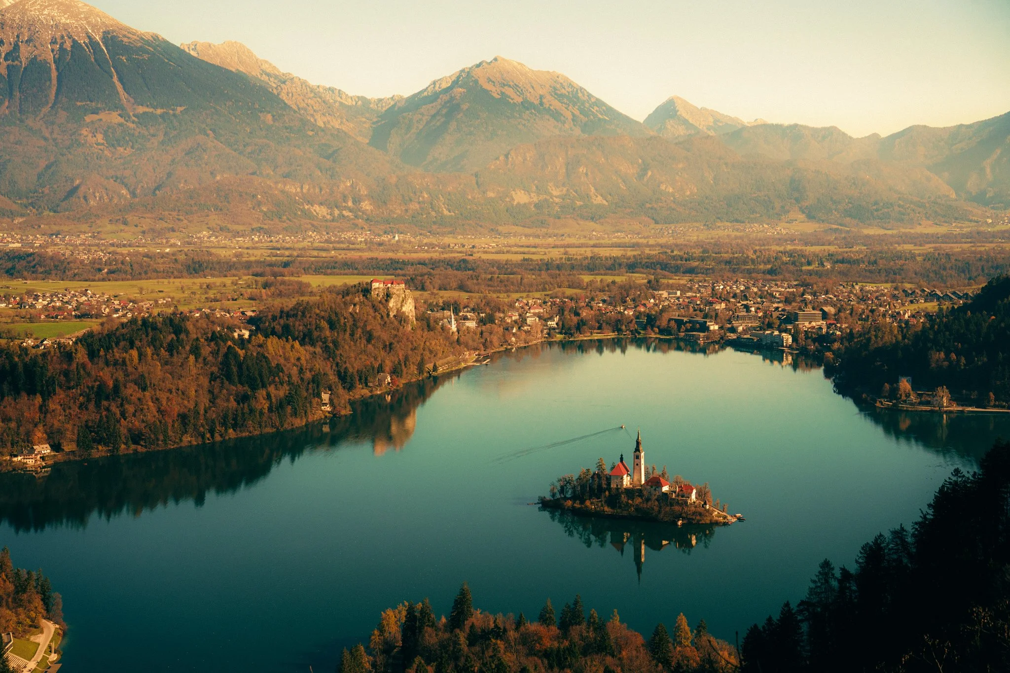 A serene lake in Slovenia with an island featuring a church and surrounding buildings, set against mountains in the background during autumn.