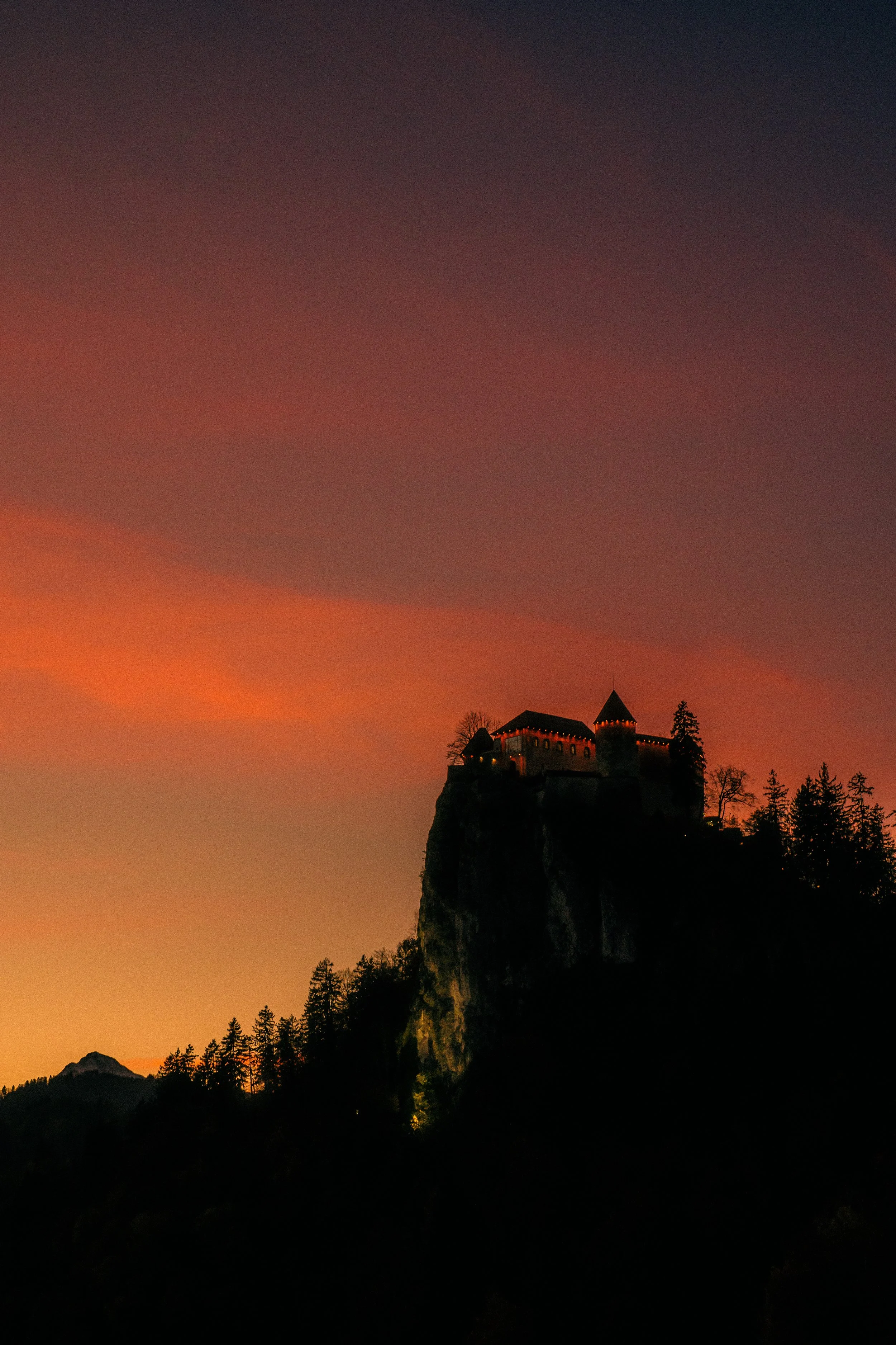 A castle silhouette atop a mountain against a vibrant sunset sky with orange, pink, purple, and blue hues.