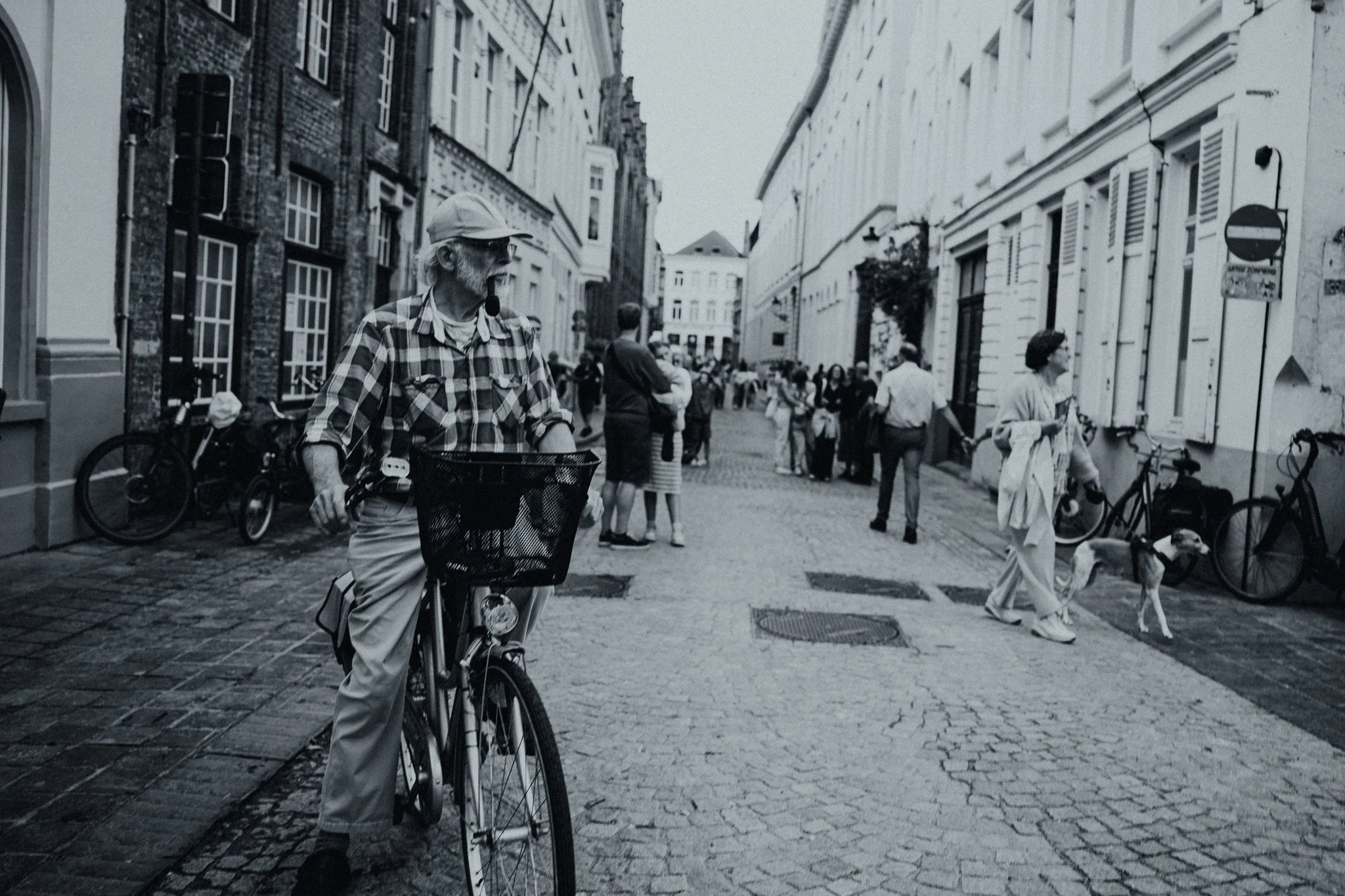A black-and-white photo of a busy cobblestone street with people walking, some with bicycles, and historic buildings in Bruges, Belgiuim.