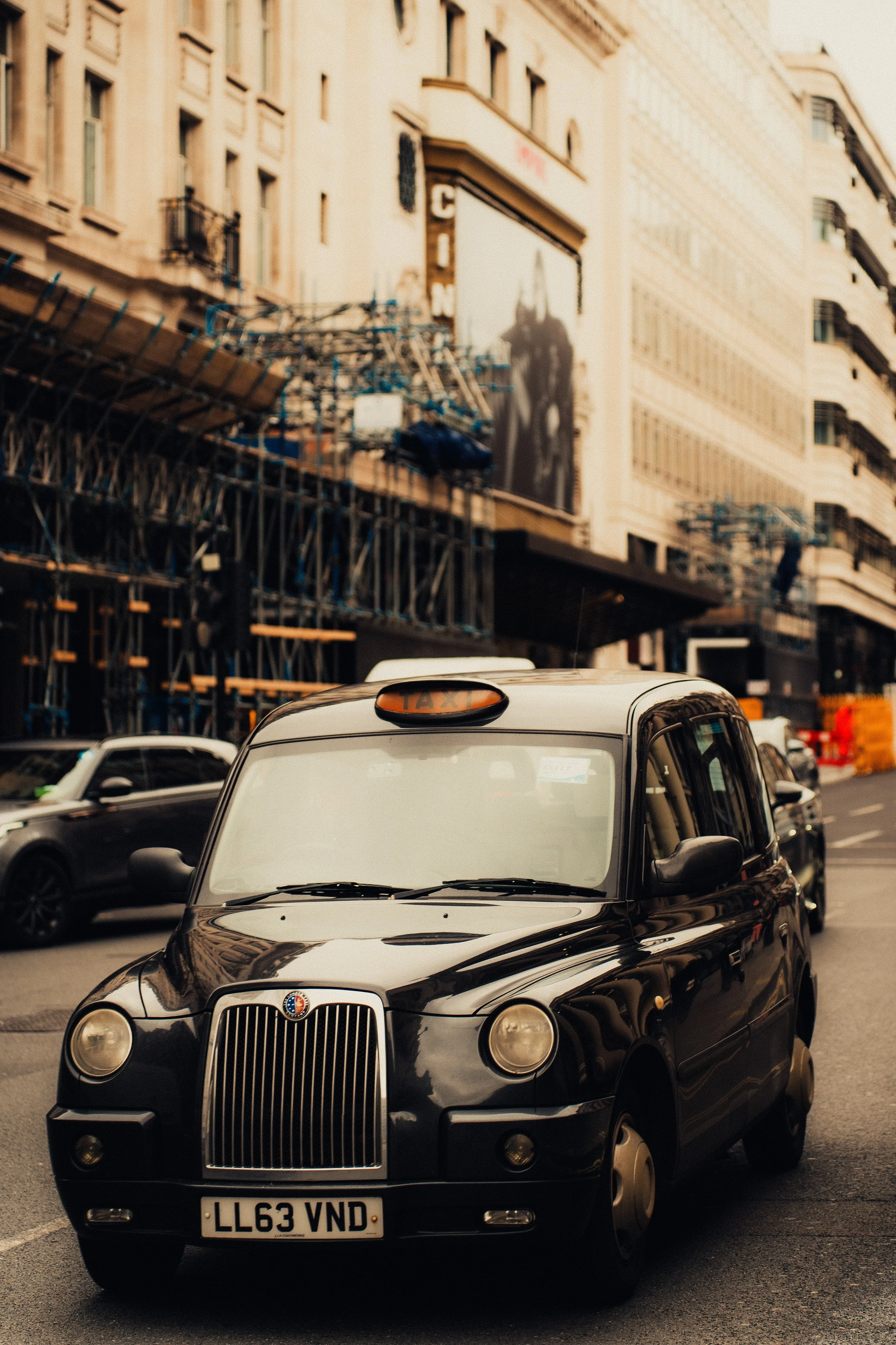 Black cab taxi on city street with buildings and construction in the background.