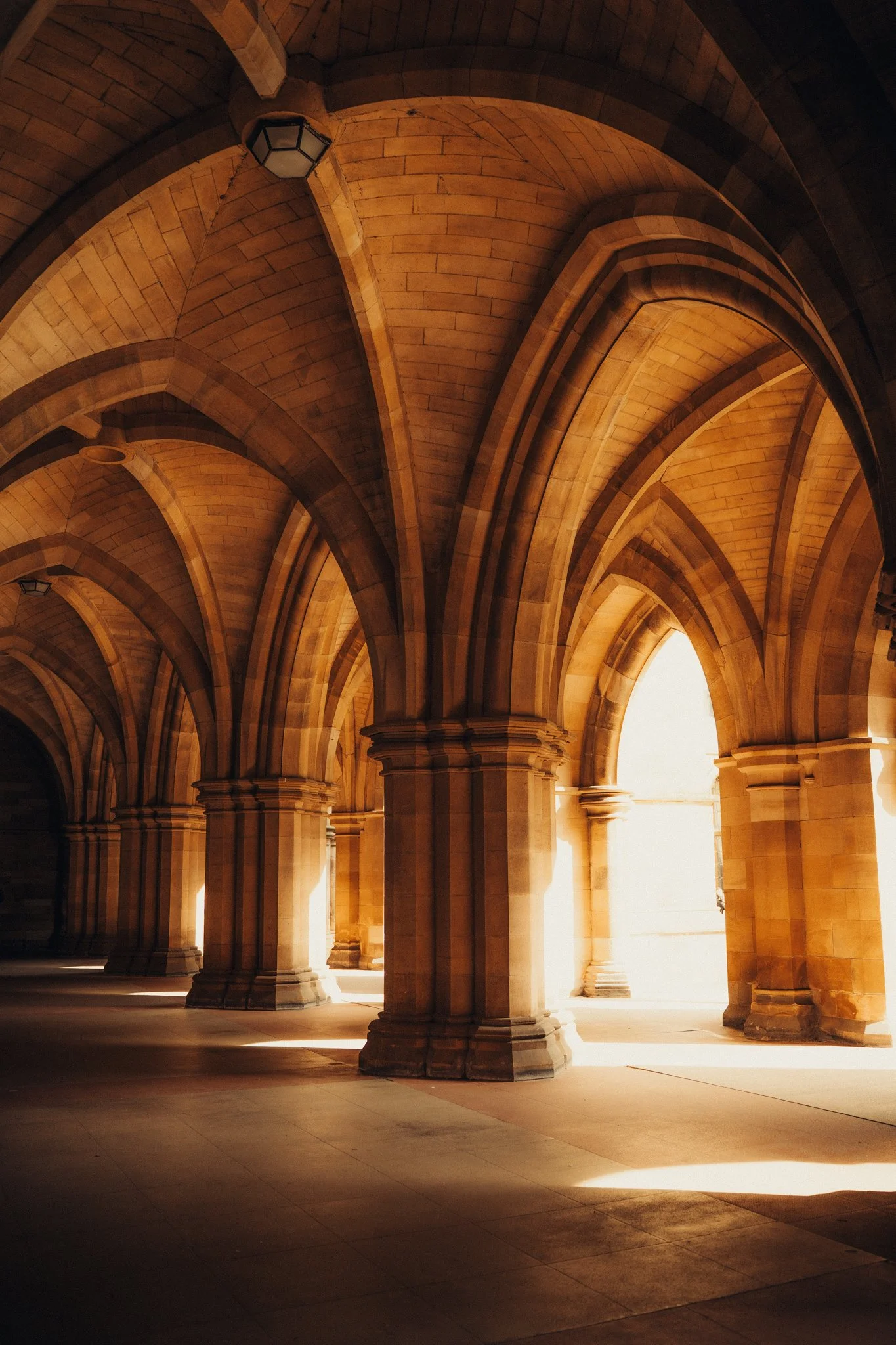 Sunlight streams through arched stone columns in a historic building exterior corridor.