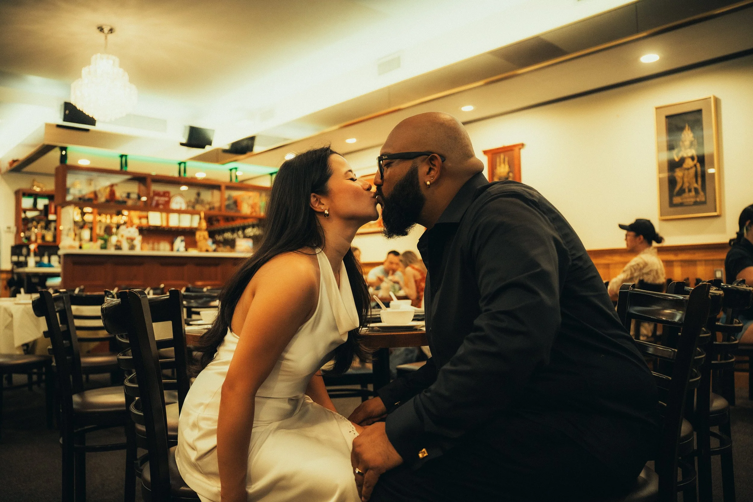 A couple kissing in a restaurant with other diners in the background.