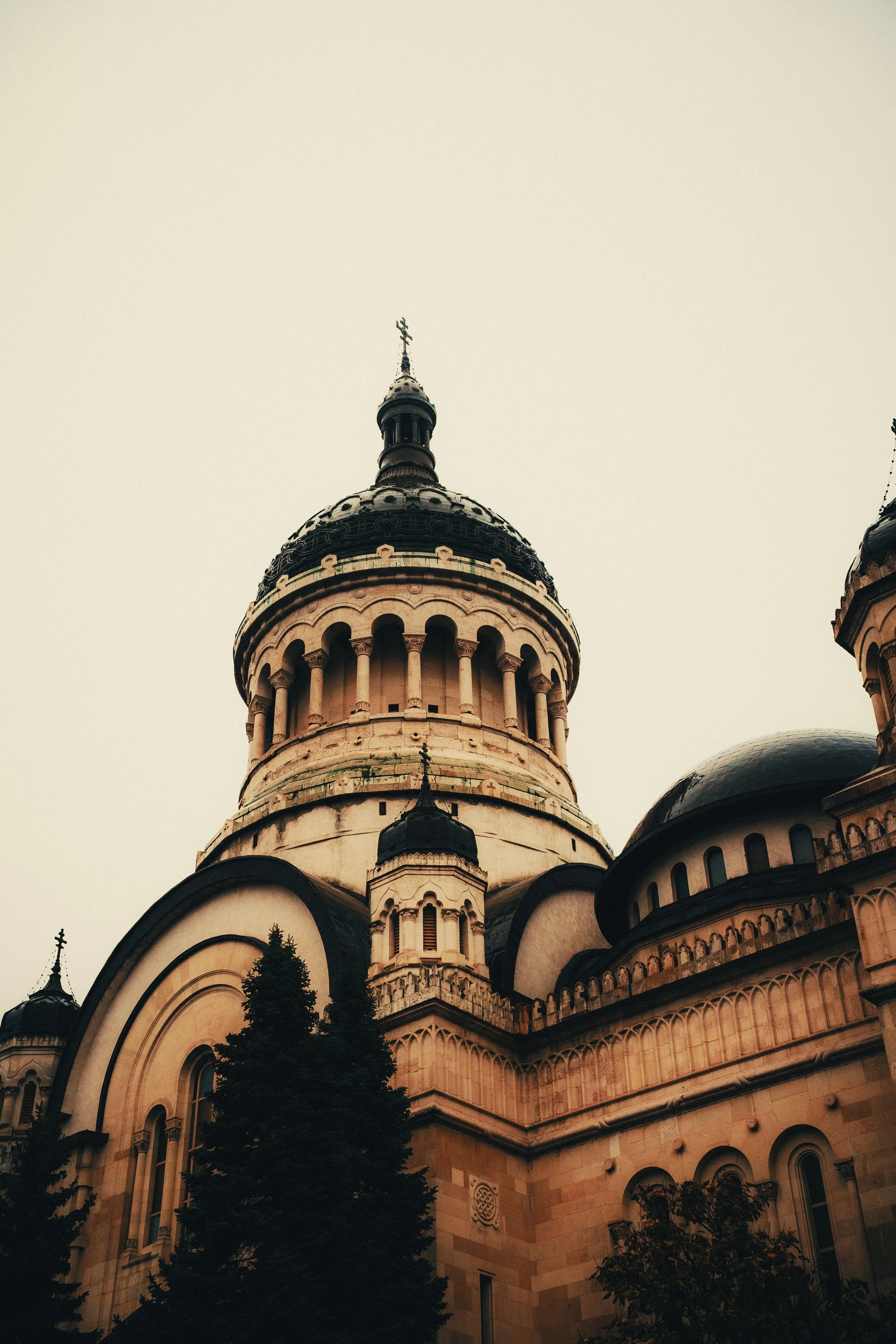 The photograph shows a majestic beige and black cathedral with a large central dome topped with a cross, surrounded by smaller domes and trees in the foreground.