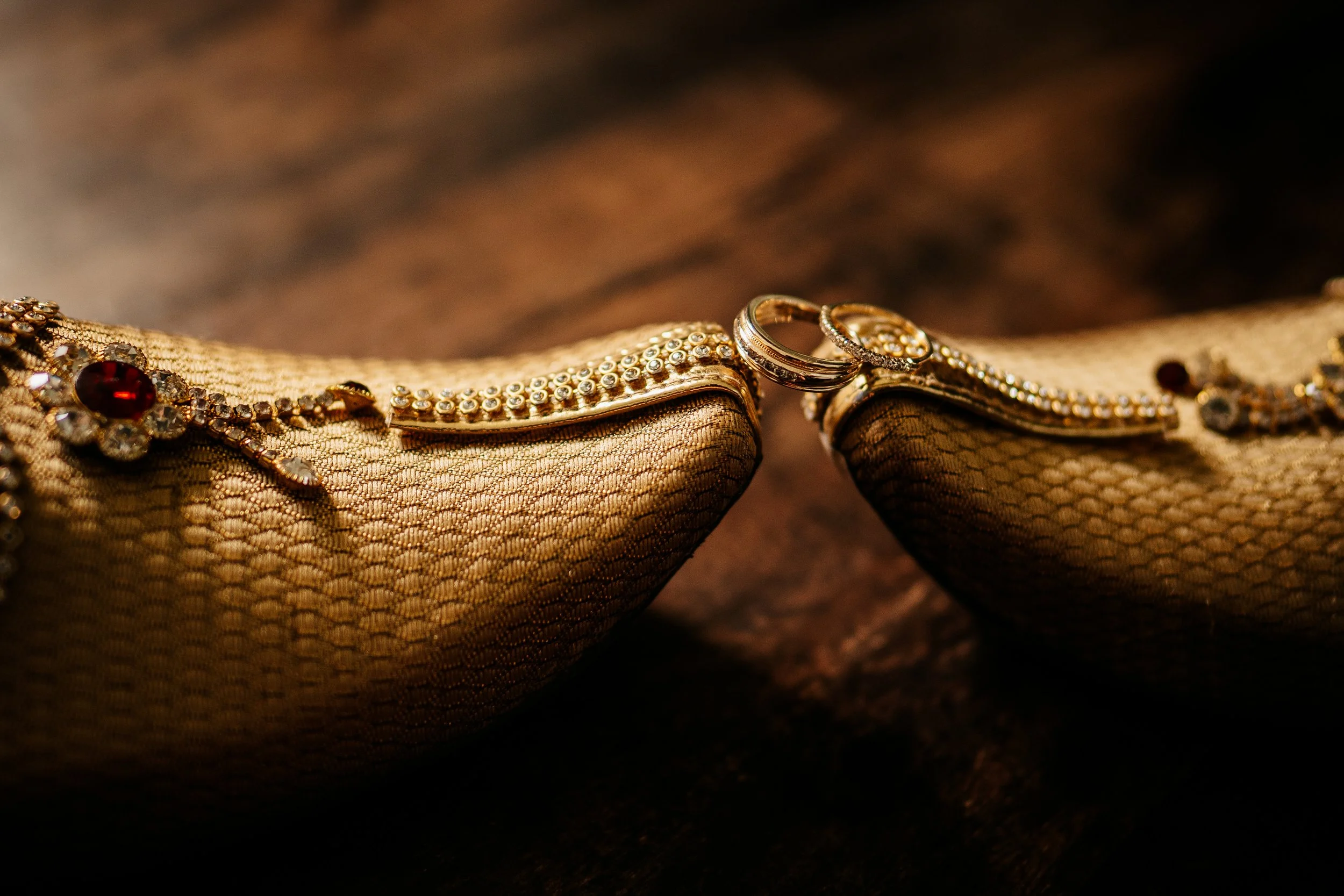 Close-up of gold jewelry, including rings and necklaces (Sri Lankan style), resting on a textured fabric surface.