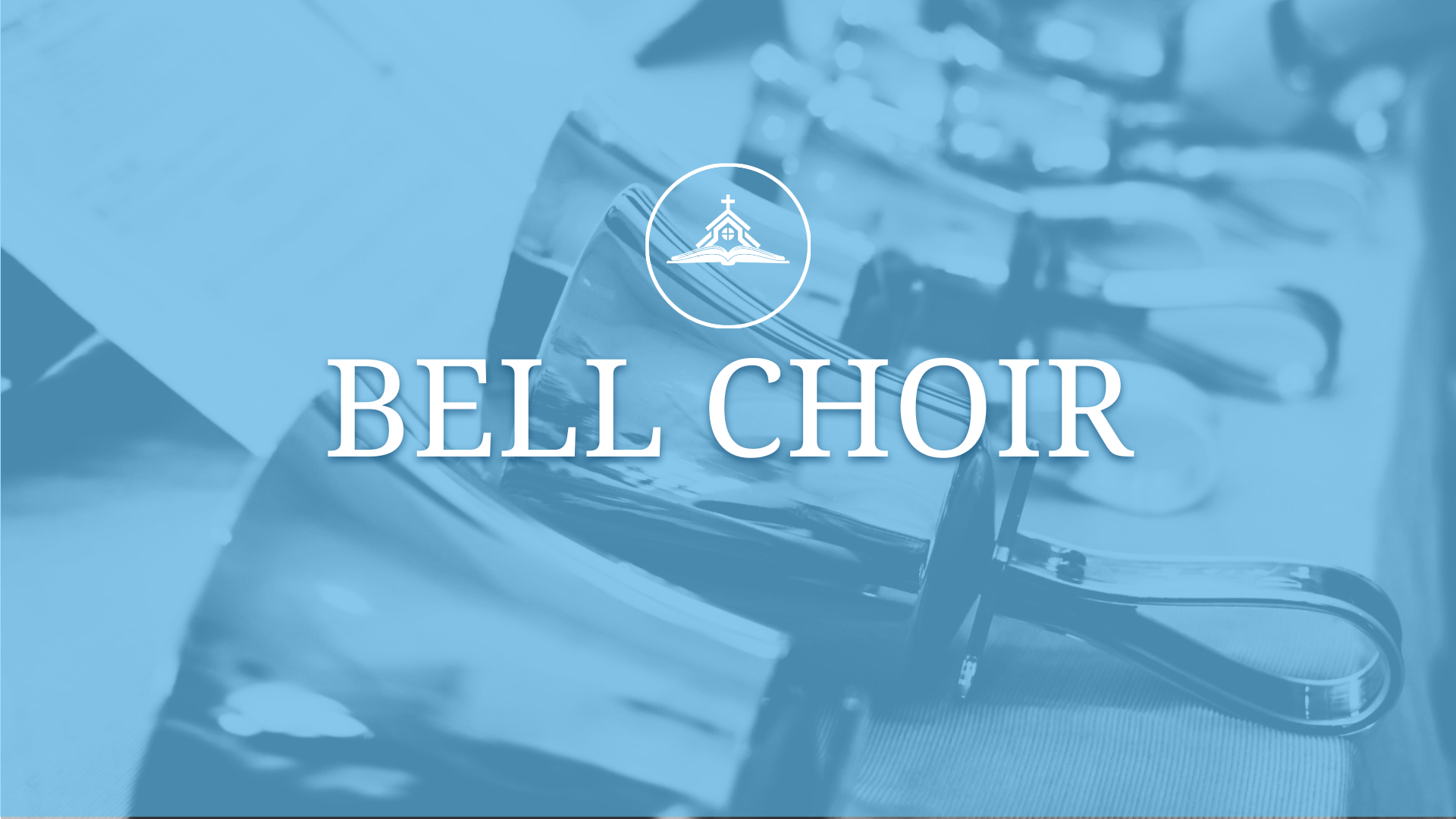 Three handbells placed on a table with sheet music and baton, in front of a yellow and white sign that says 'Handbell Choir'.
