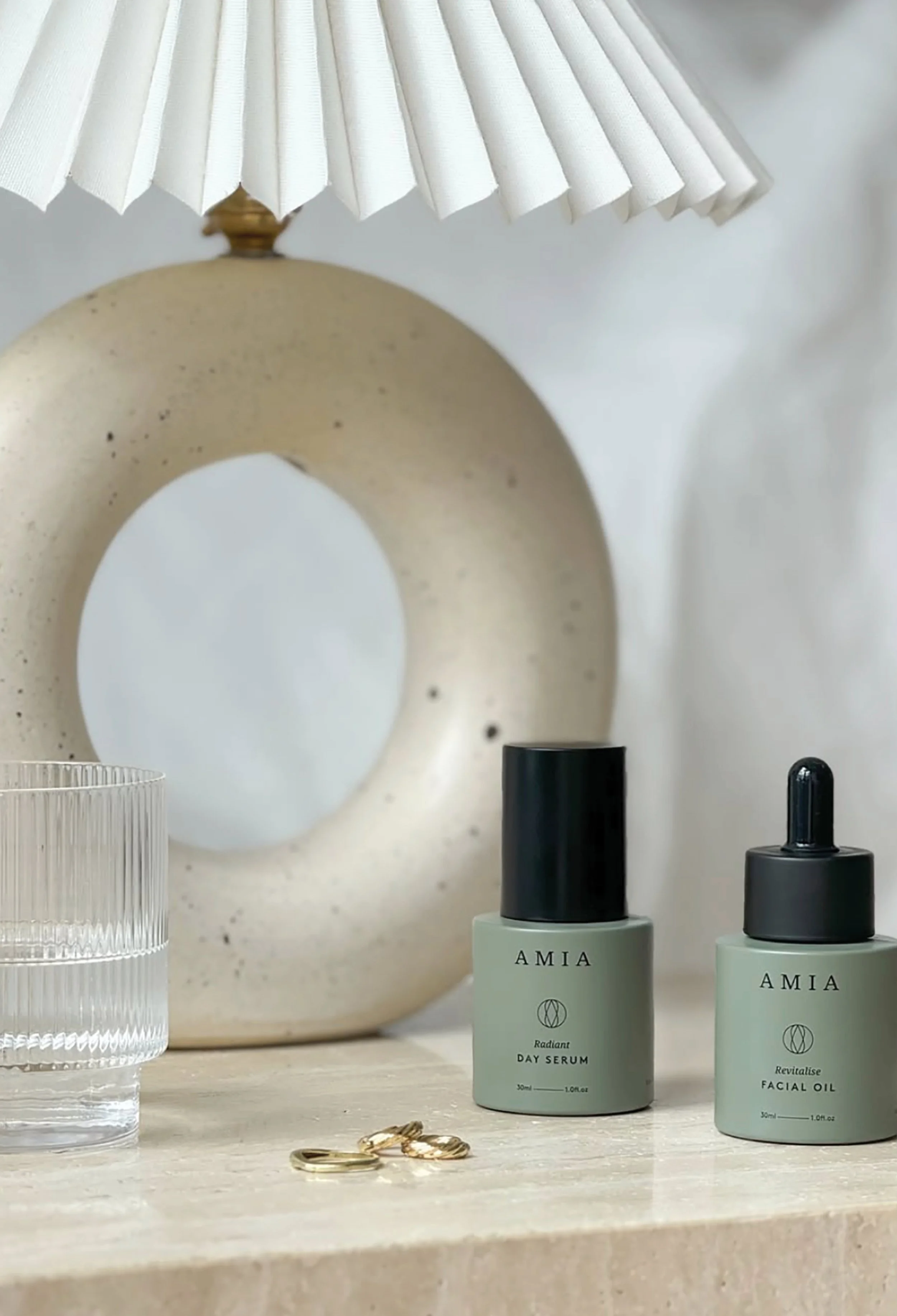 Image of Amia Skincare products on table with lamp, glass of water and jewellery