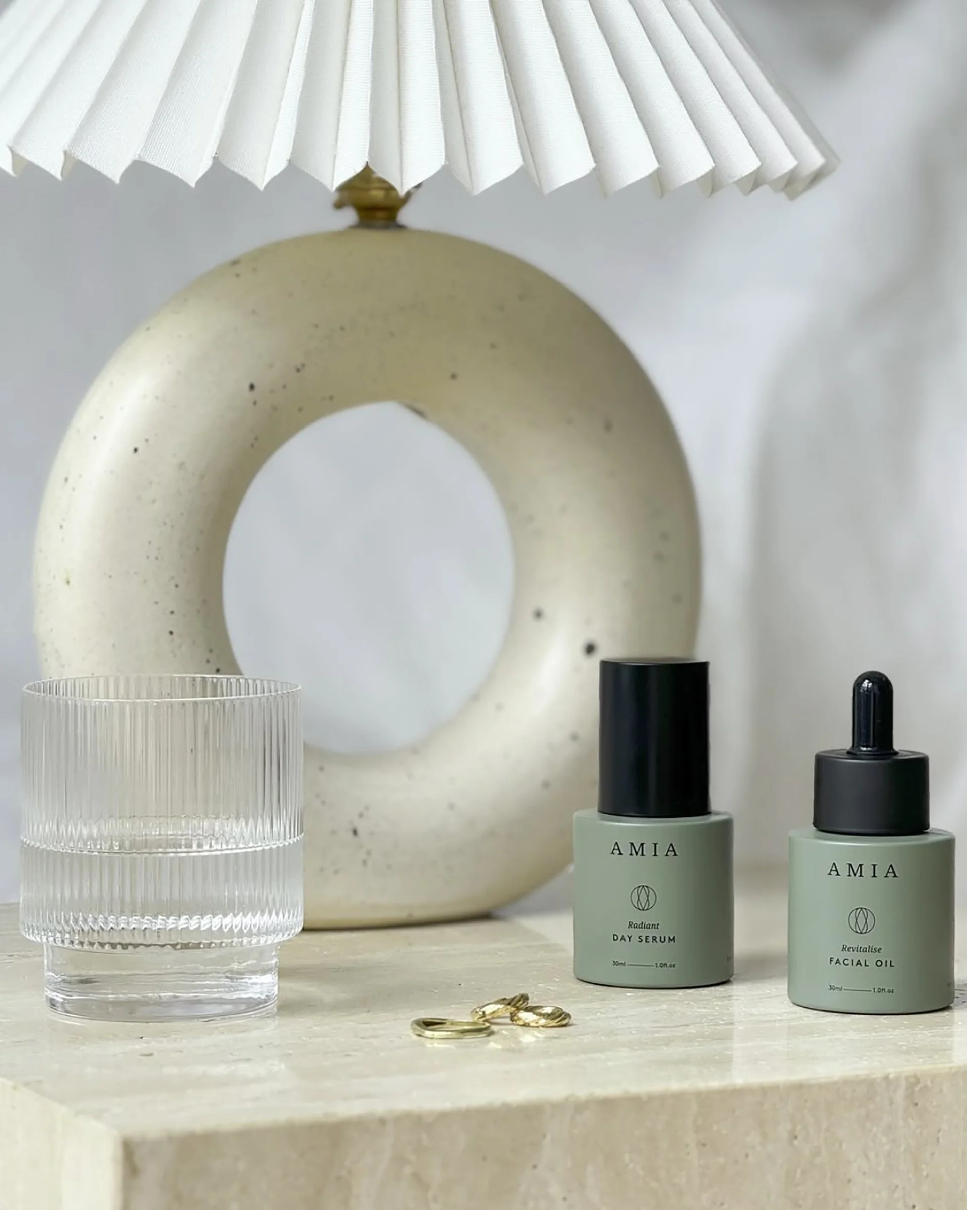 Image of Amia Skincare packaging on table with jewellery, a glass and a lamp
