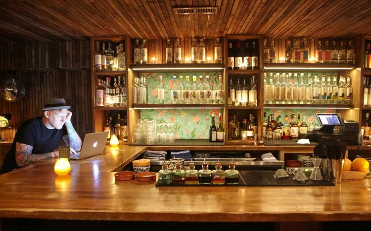 Quiote by Siren Betty Design. Bar detail with mezcal bottles, floral back bar pattern, and a warm wood counter.