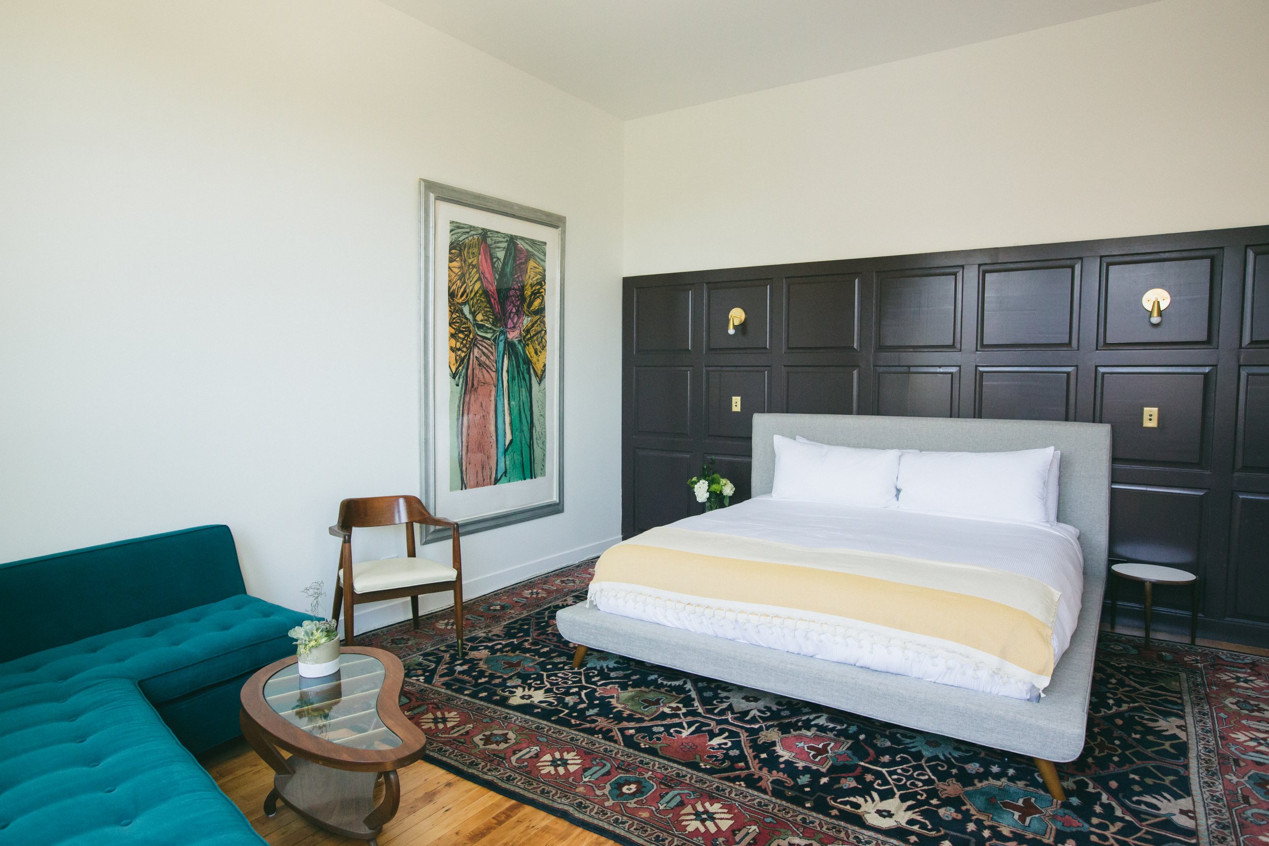 The Publishing House guest suite with dark paneled walls, a teal sectional, vintage rugs, and midcentury furnishings by Siren Betty Design.