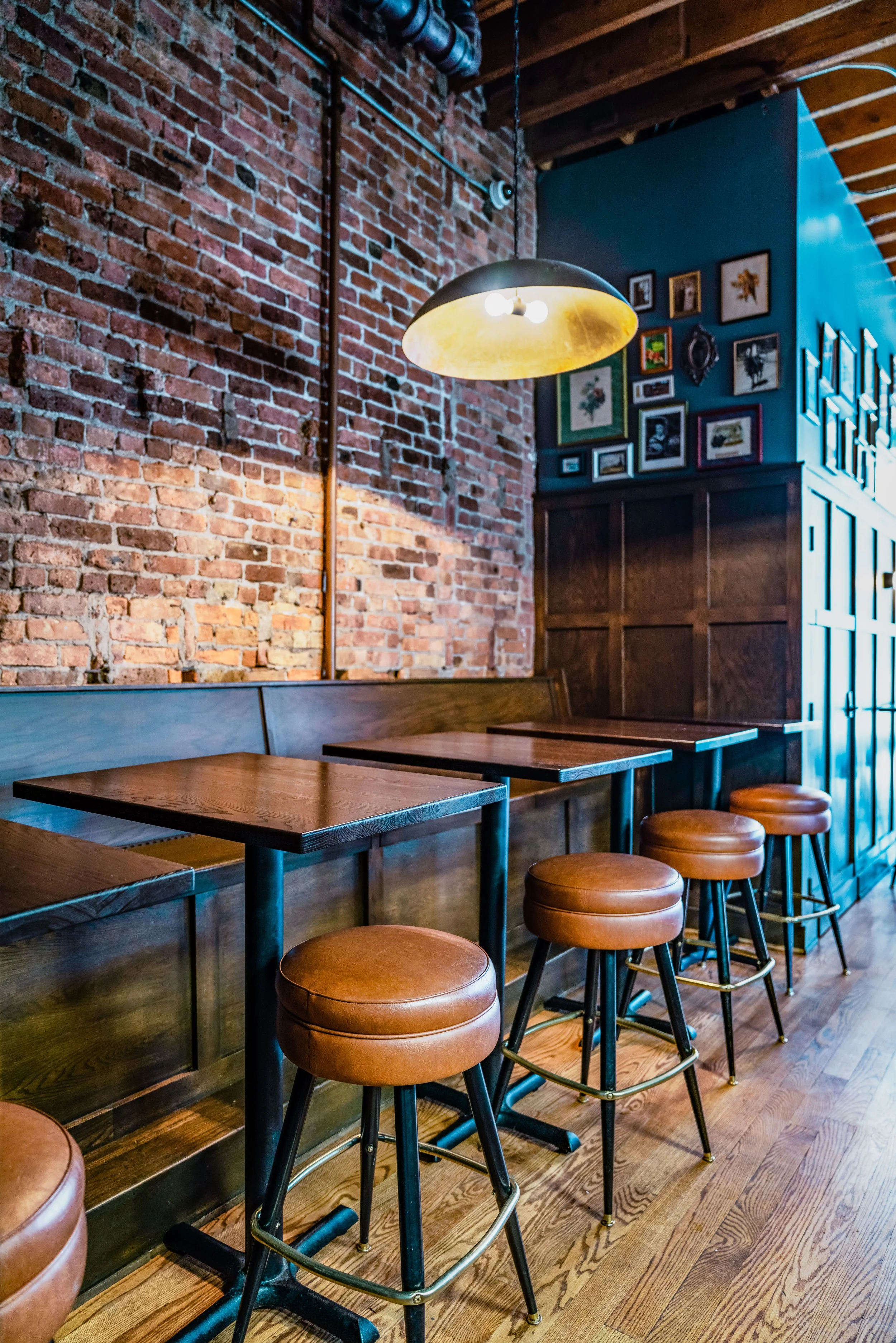 The Swill Inn by Siren Betty Design, warm tavern seating with brick walls, wood paneling, and leather stools.